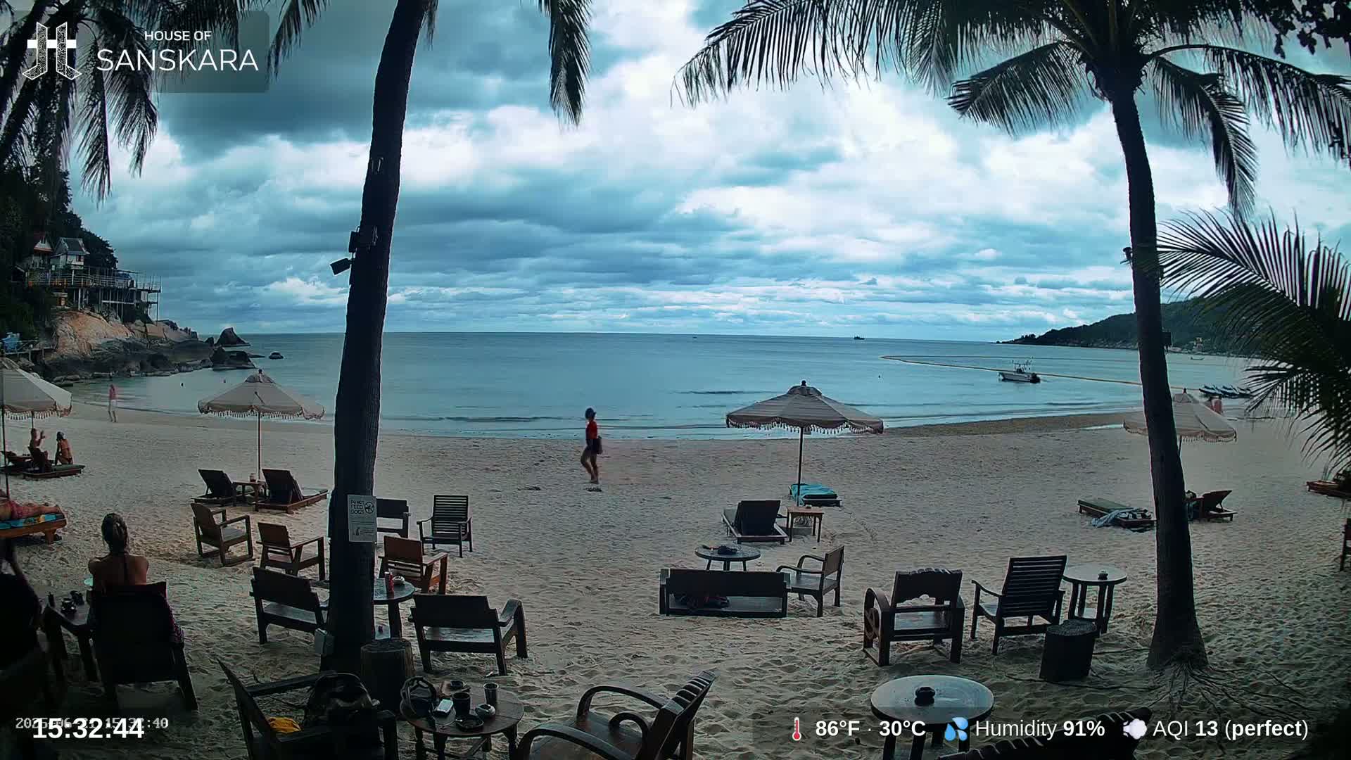 A sandy beach with palm trees, lounge chairs, and umbrellas under a partly cloudy sky overlooks a calm ocean.