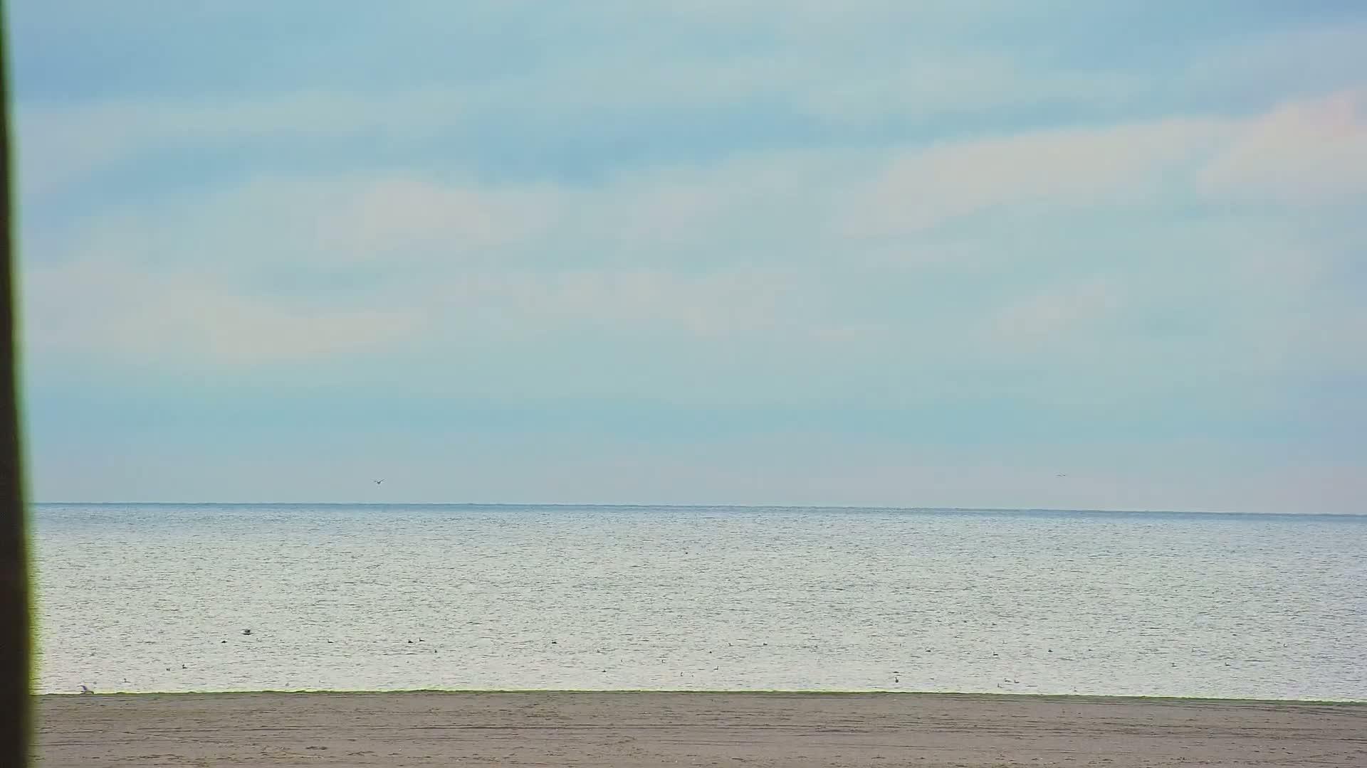 A calm ocean with a light-blue sky above a sandy beach.