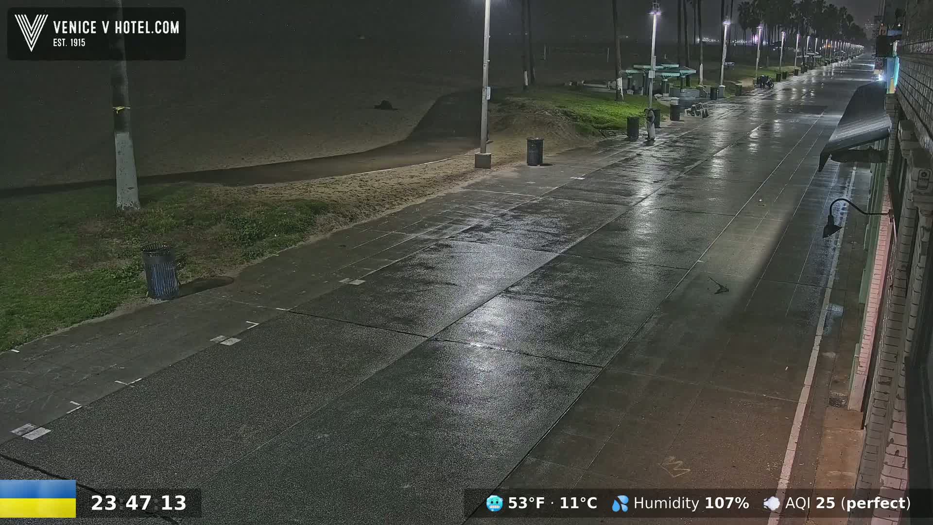 A wet nighttime boardwalk stretches toward the beach under illuminated streetlights.