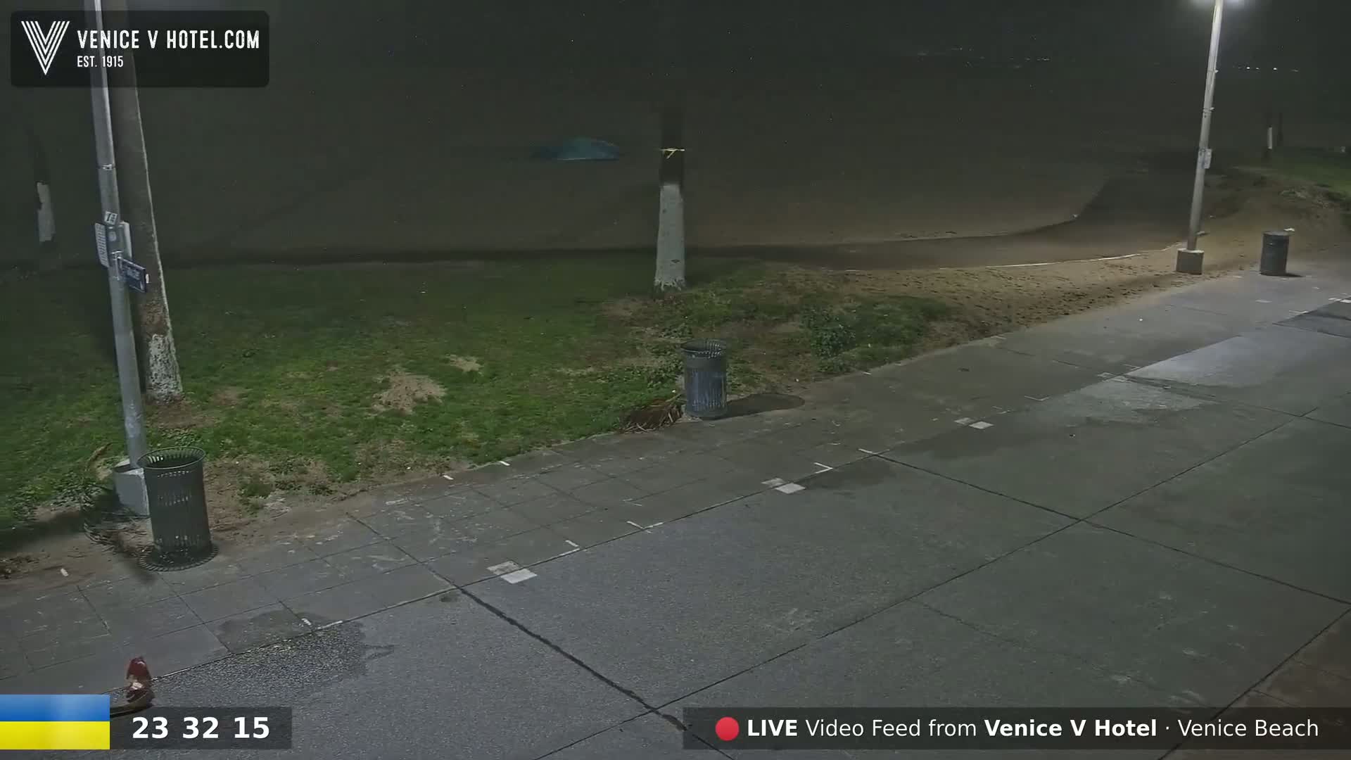 A nighttime view of a sidewalk next to a grassy area and sandy beach under hazy conditions.
