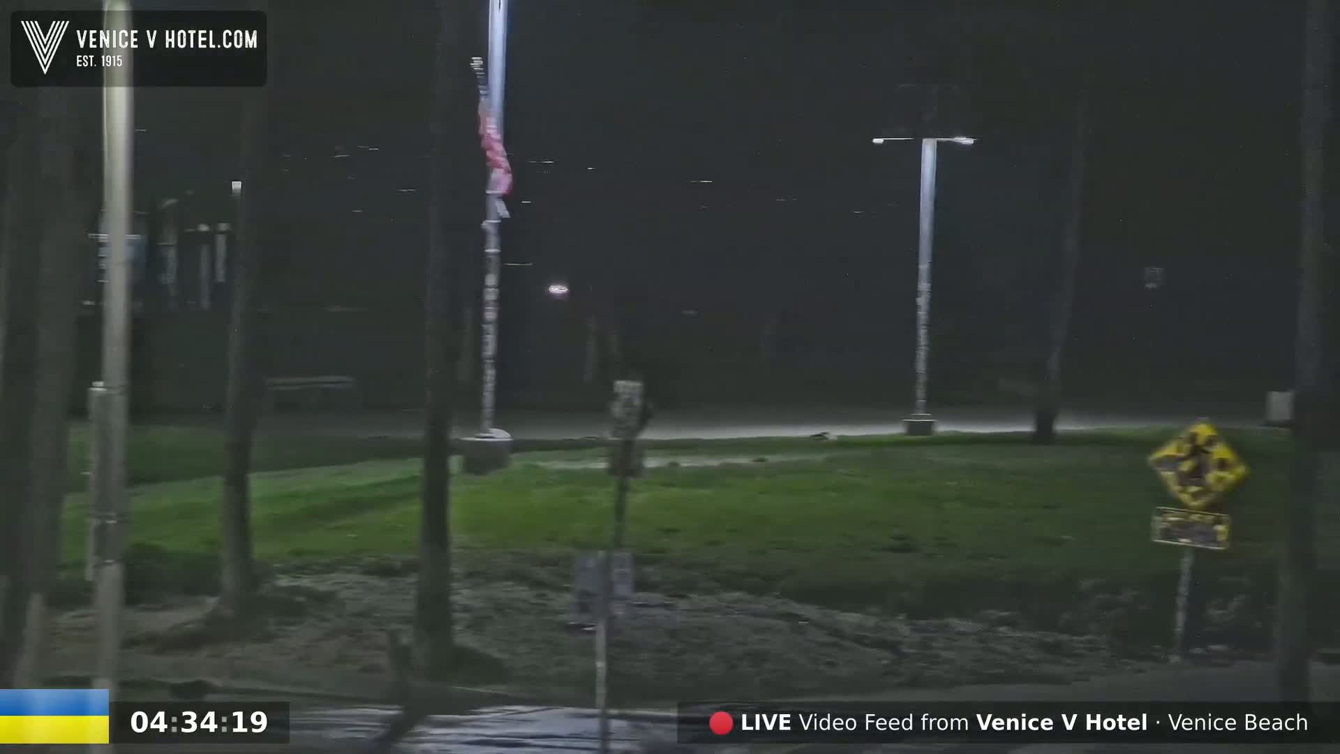 A nighttime, outdoor scene shows a grassy area with lampposts and a flagpole, under dark, possibly rainy conditions.