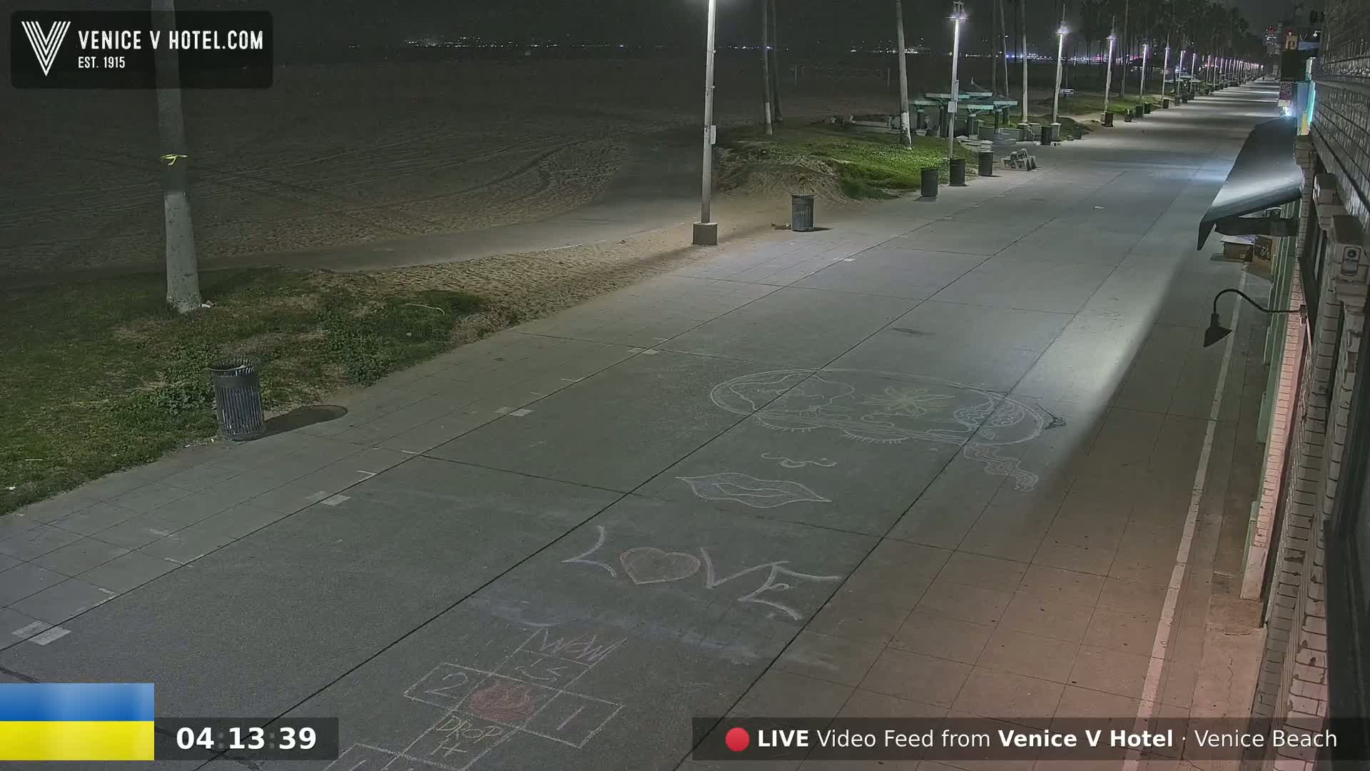 A nighttime view of a mostly empty boardwalk next to a sandy beach, with chalk drawings on the pavement.