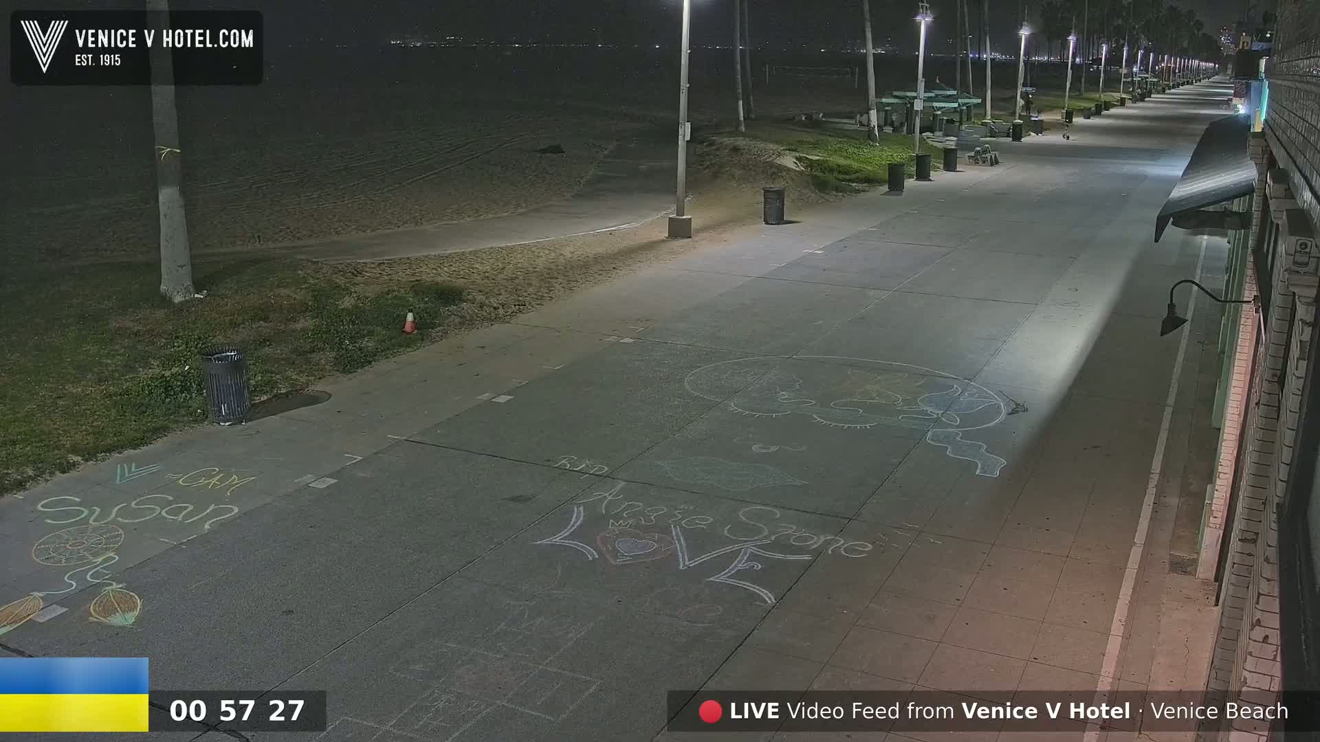 A nighttime view of a beach boardwalk with chalk drawings on the pavement, under mostly clear skies.