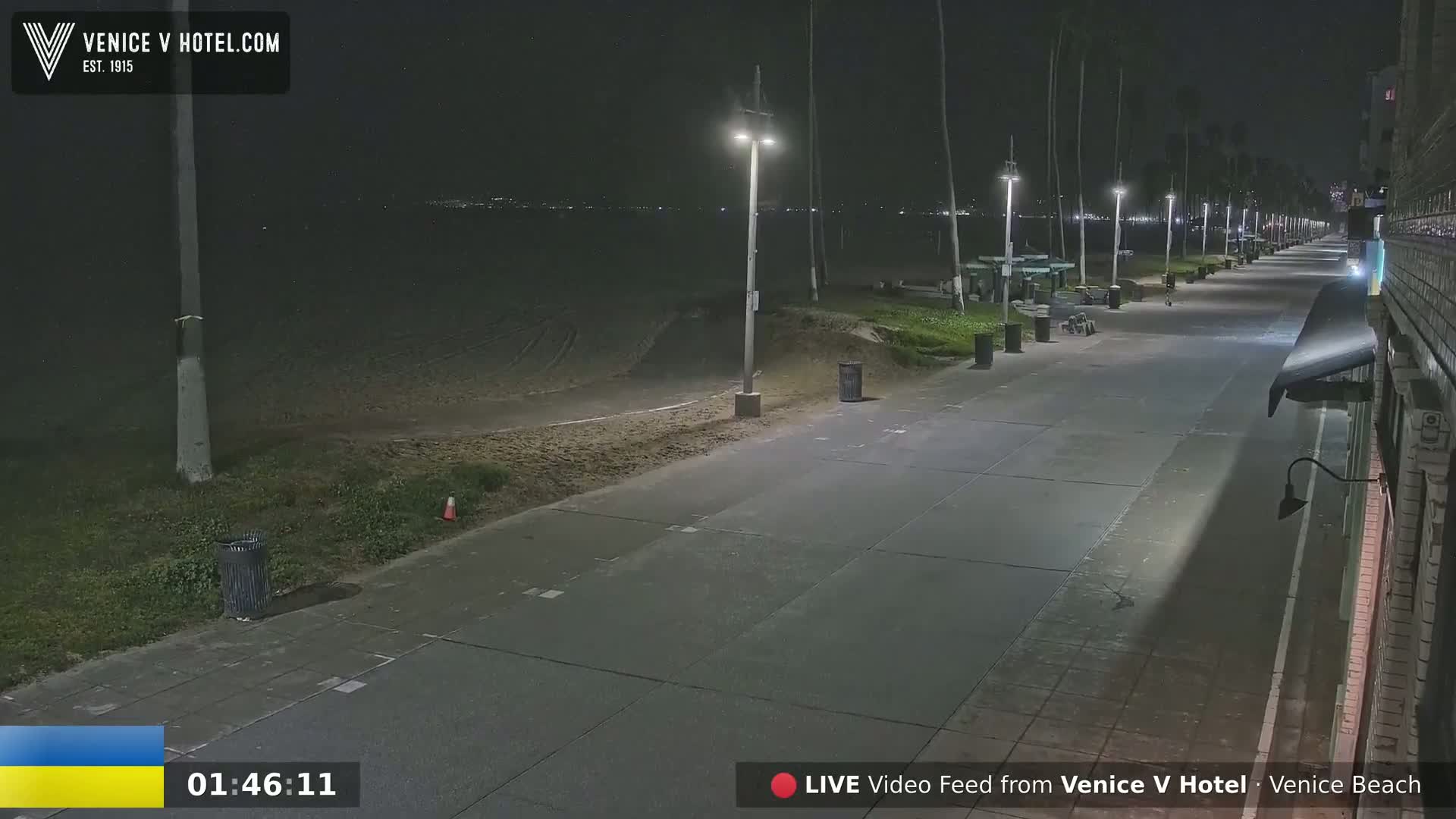 A nighttime view of a mostly empty beach boardwalk, lit by streetlights, next to a dark ocean.