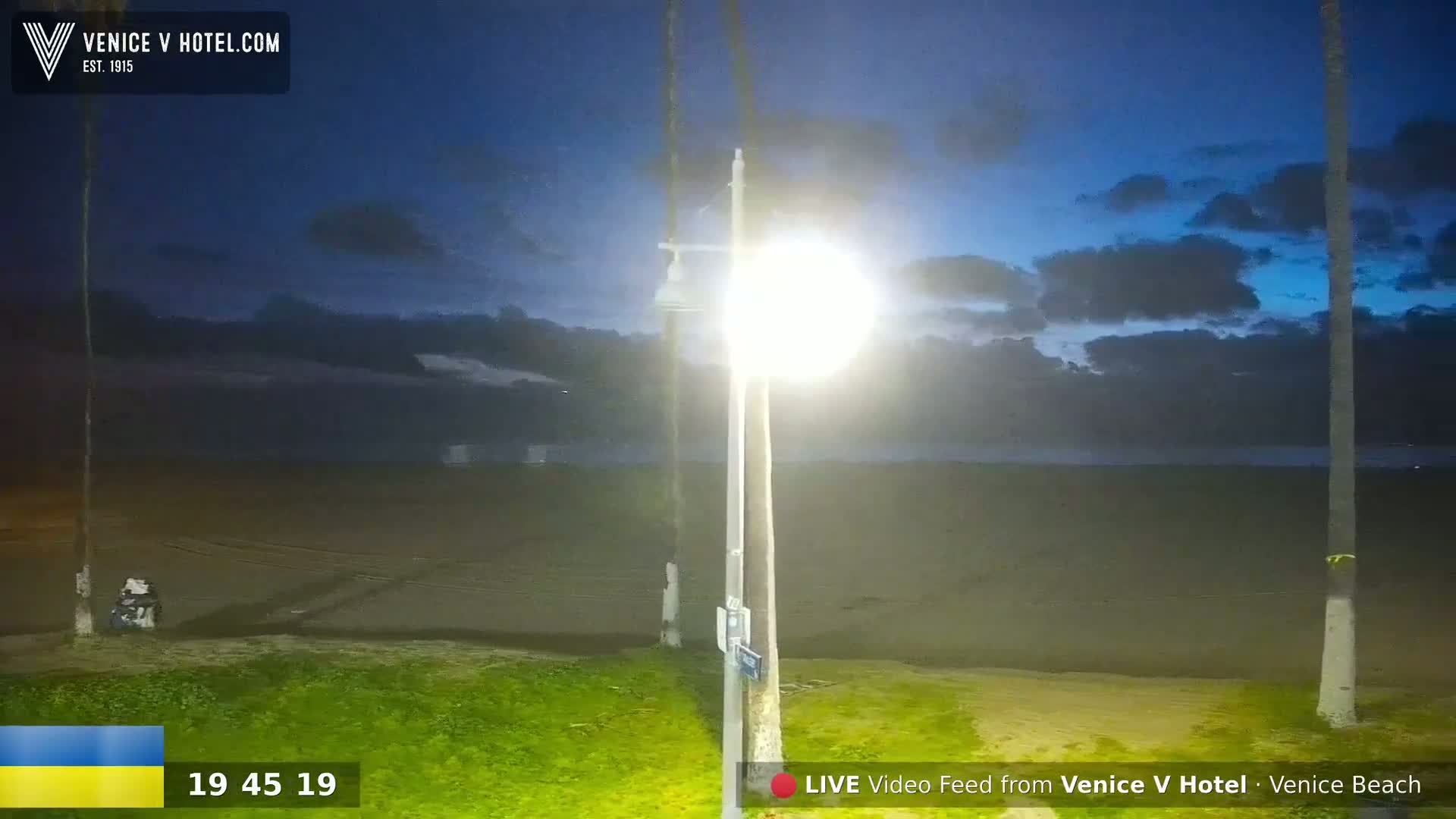 A bright lamp illuminates a dark beach at twilight under a partly cloudy sky.