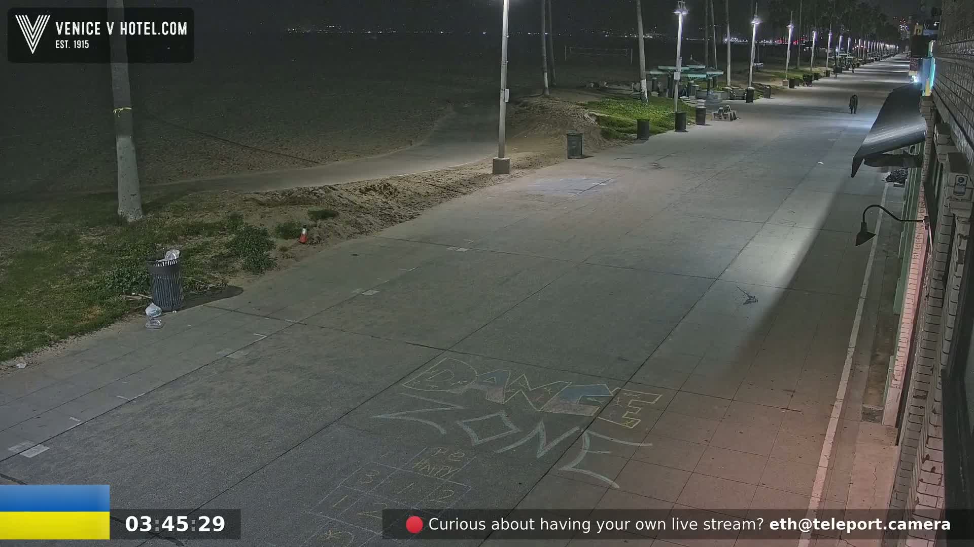 A nighttime, deserted beach boardwalk with chalk drawings on the pavement, lit by streetlights.