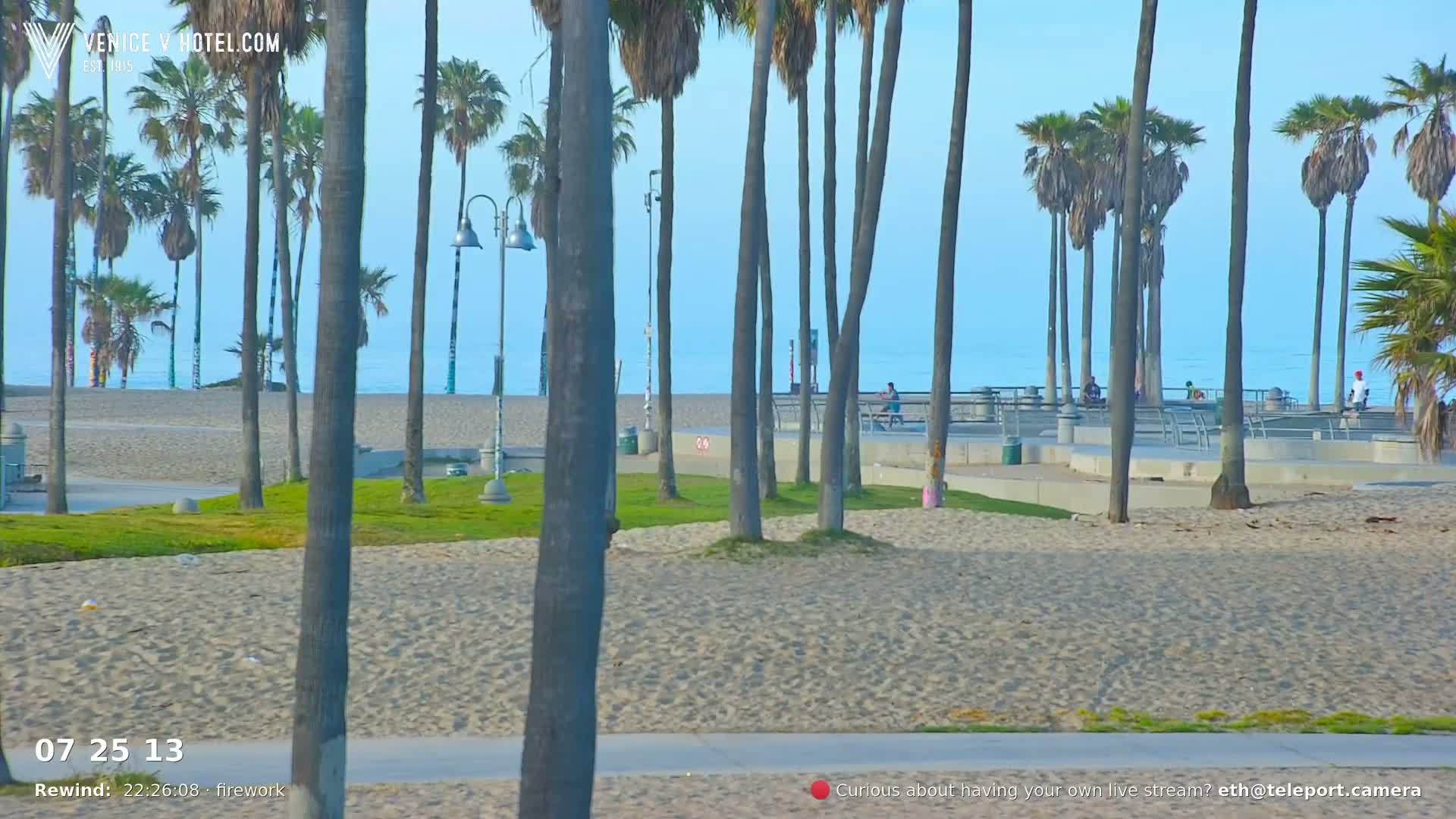 A sandy beach with palm trees, a paved walkway, and a calm ocean under a clear sky is visible.