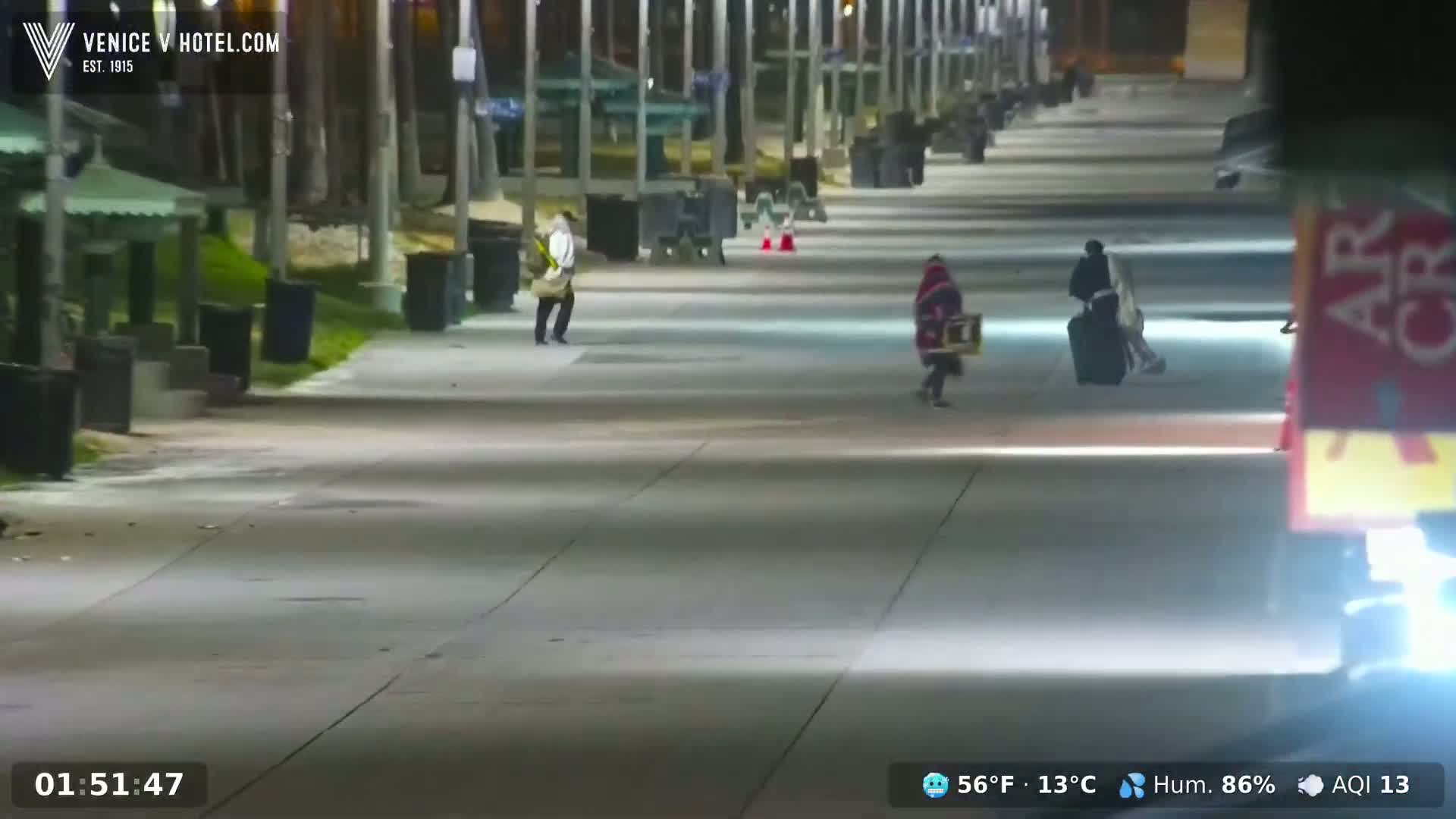A mostly empty, well-lit boardwalk at night, with a few pedestrians walking, under a clear sky with a temperature of 56°F (13°C) and 86% humidity.