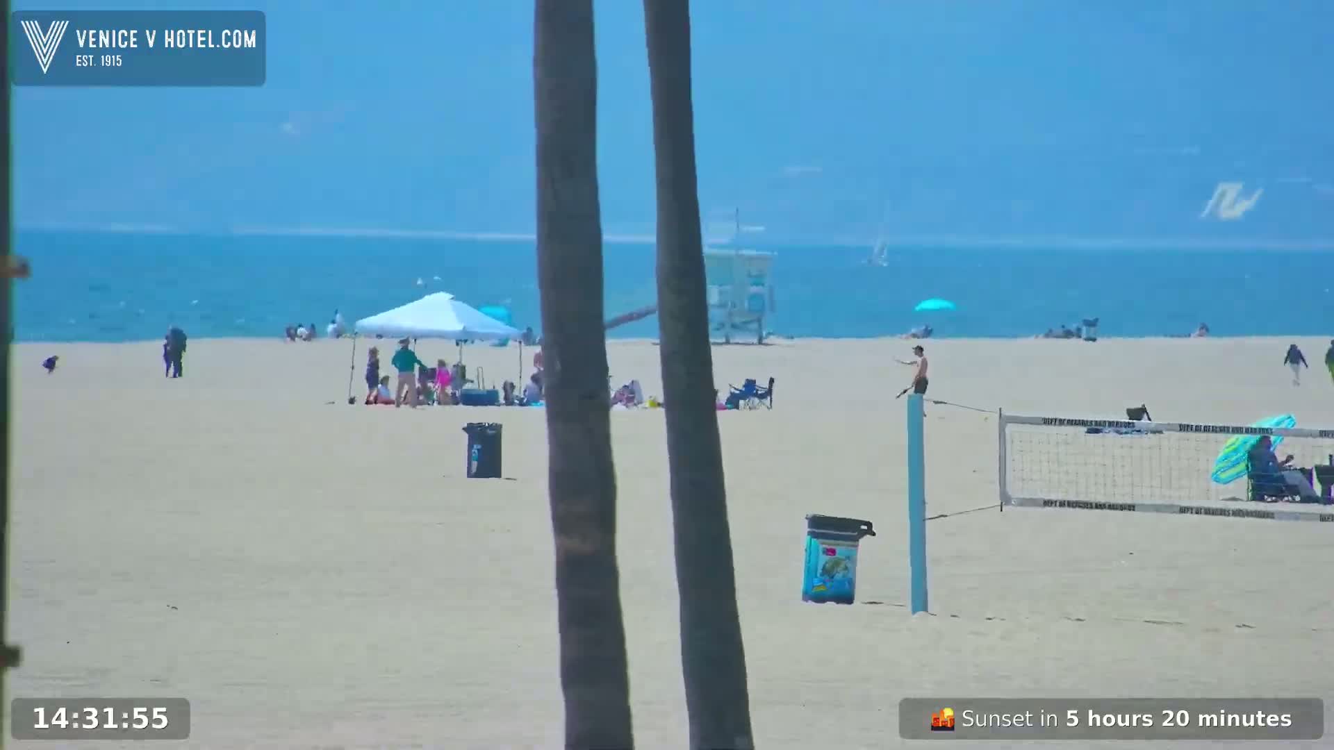 A sunny beach scene shows people relaxing under umbrellas, playing volleyball, and swimming in the ocean.