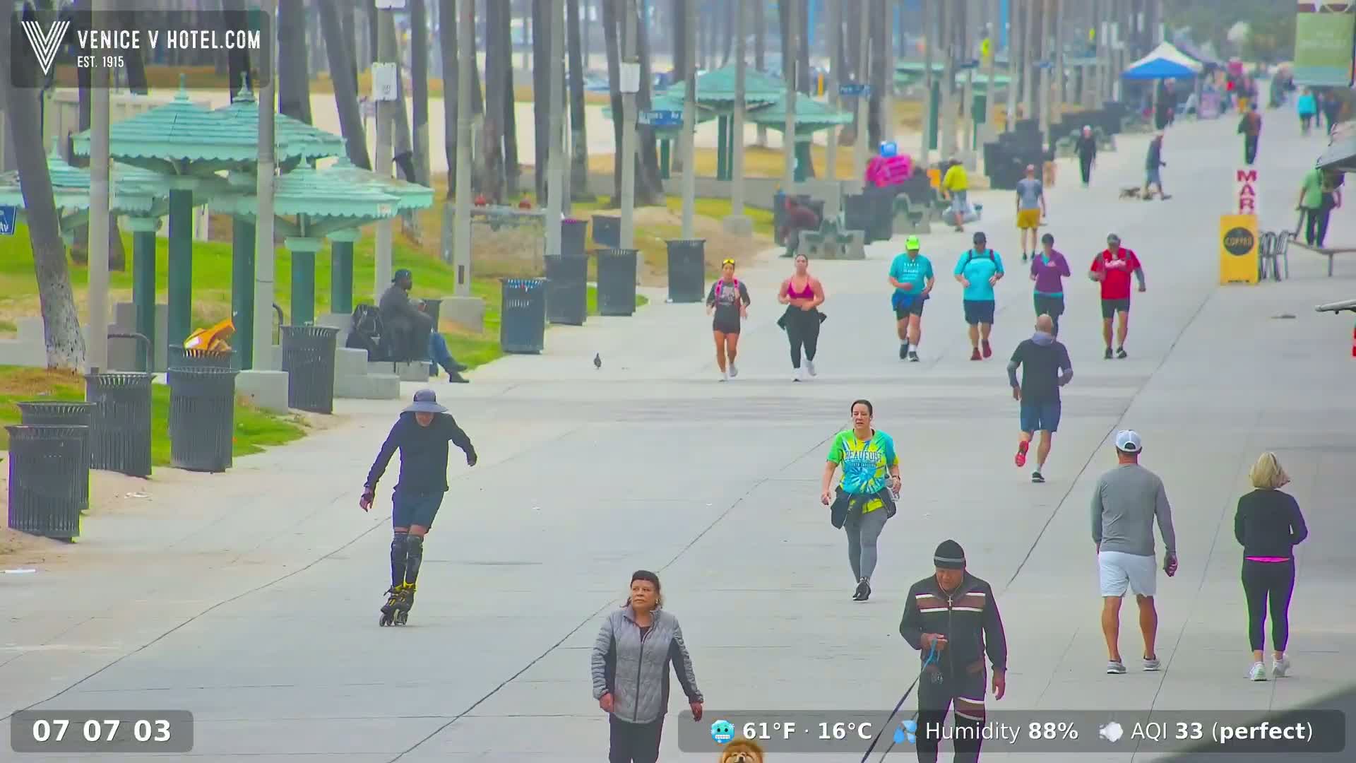 A person rollerblades along a beachfront boardwalk where many people are walking and jogging in hazy weather.