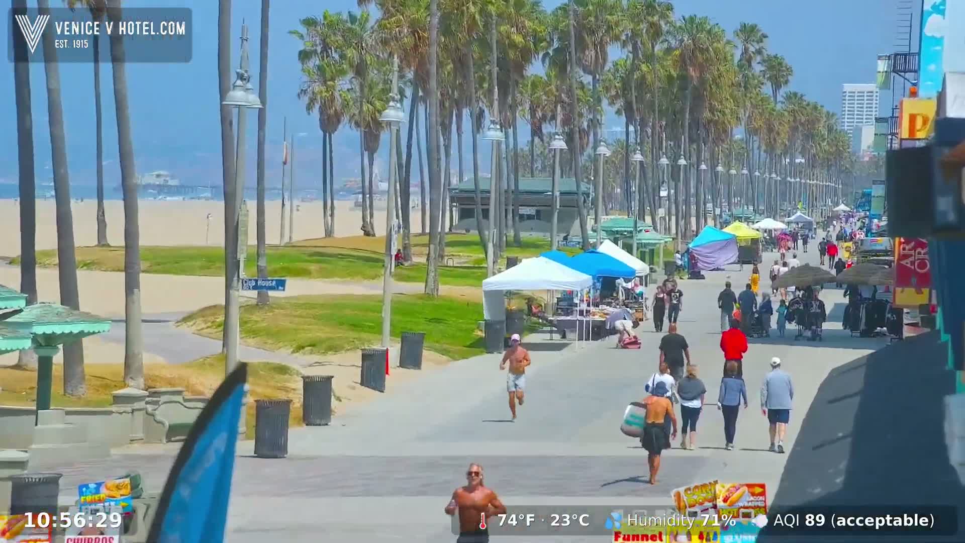 A sunny beach boardwalk scene shows people walking, some running, and vendors selling goods under sunny skies.