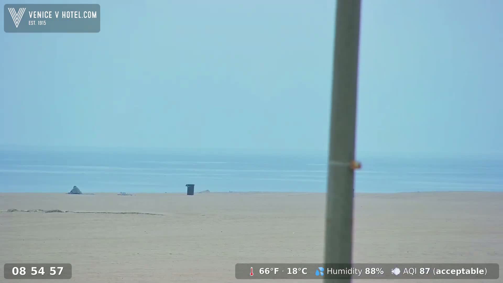 A hazy, light-blue ocean is visible beyond a wide, sandy beach with a single trash can near the center.