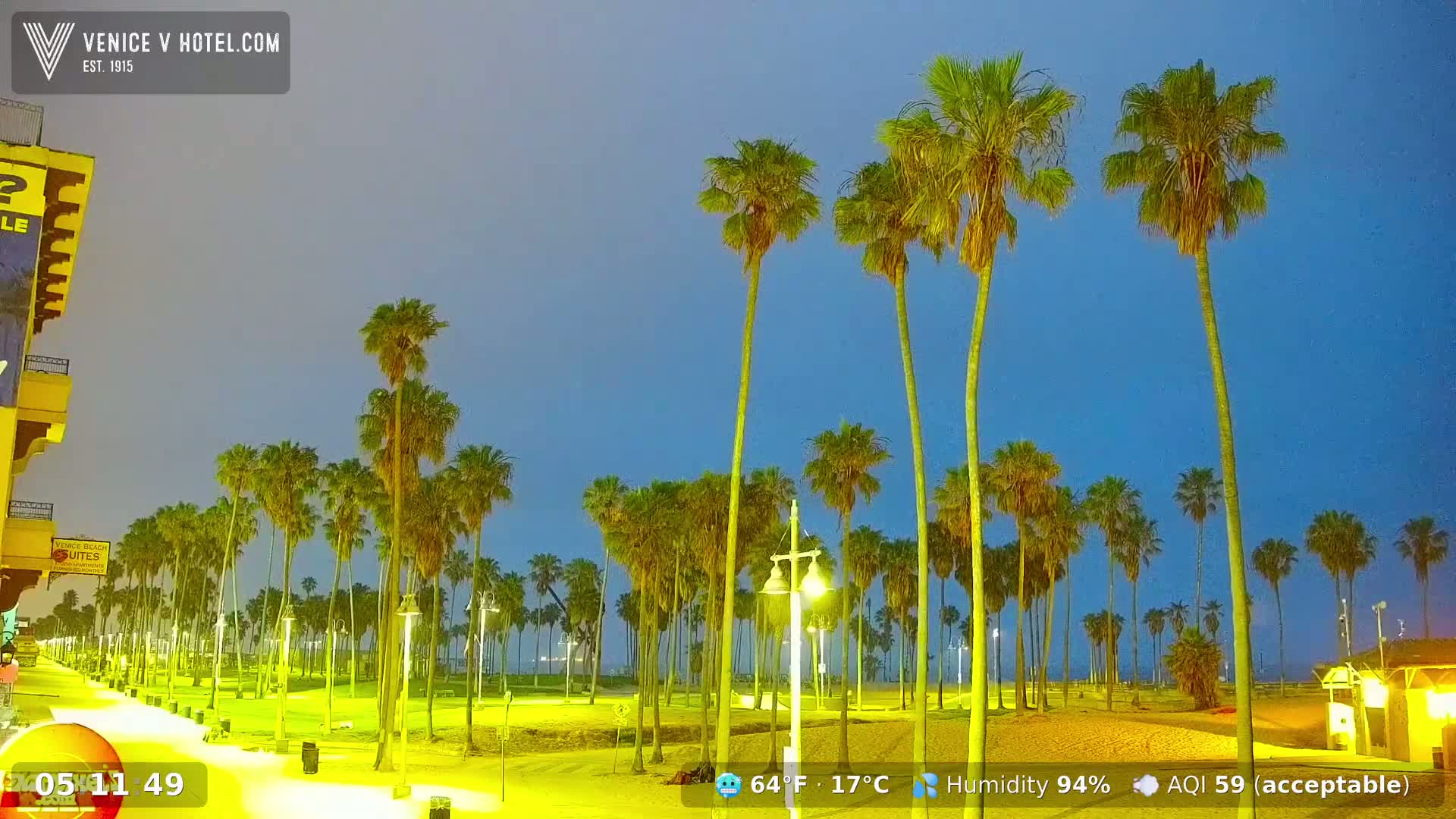 A nighttime beach scene shows a boardwalk lined with palm trees under a twilight sky with high humidity.