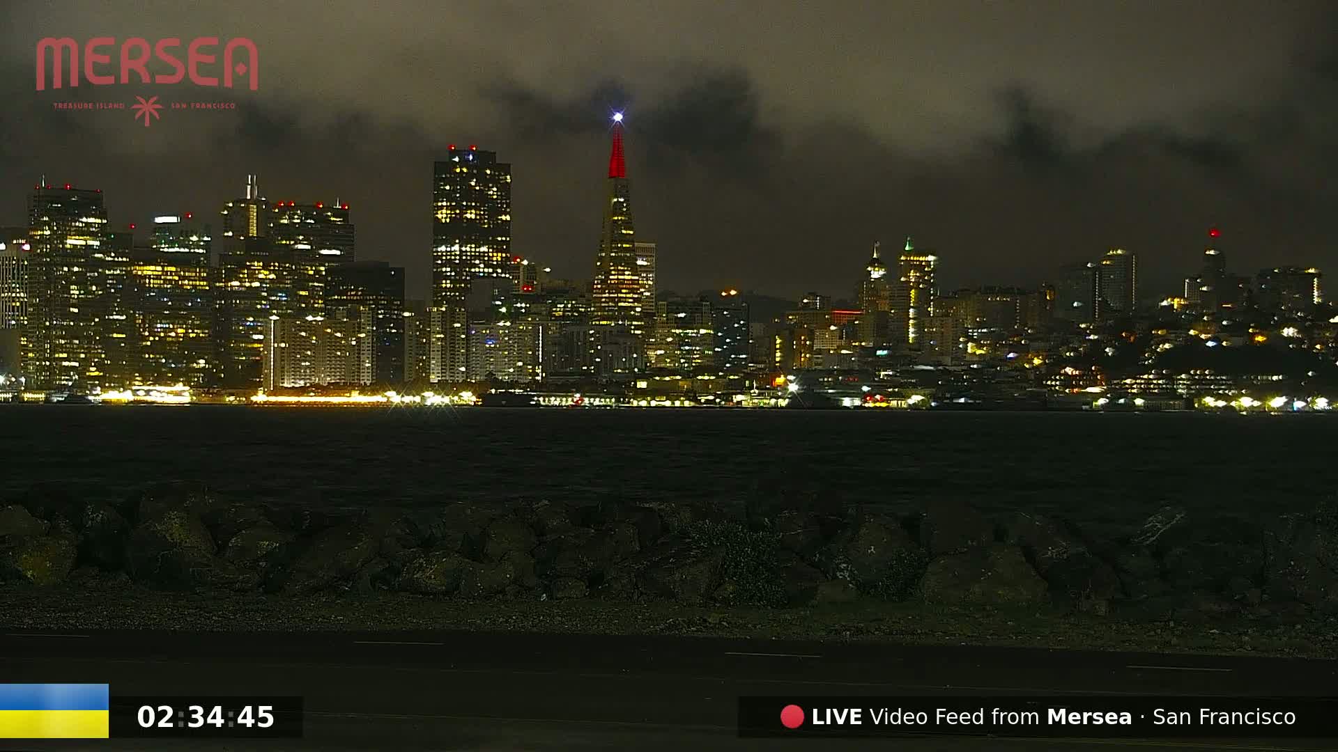 A nighttime view of a city skyline across a dark body of water under a cloudy sky.