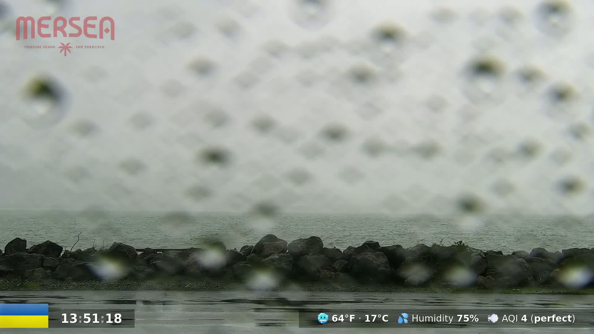 Rain falls on a rocky shoreline and overcast ocean.