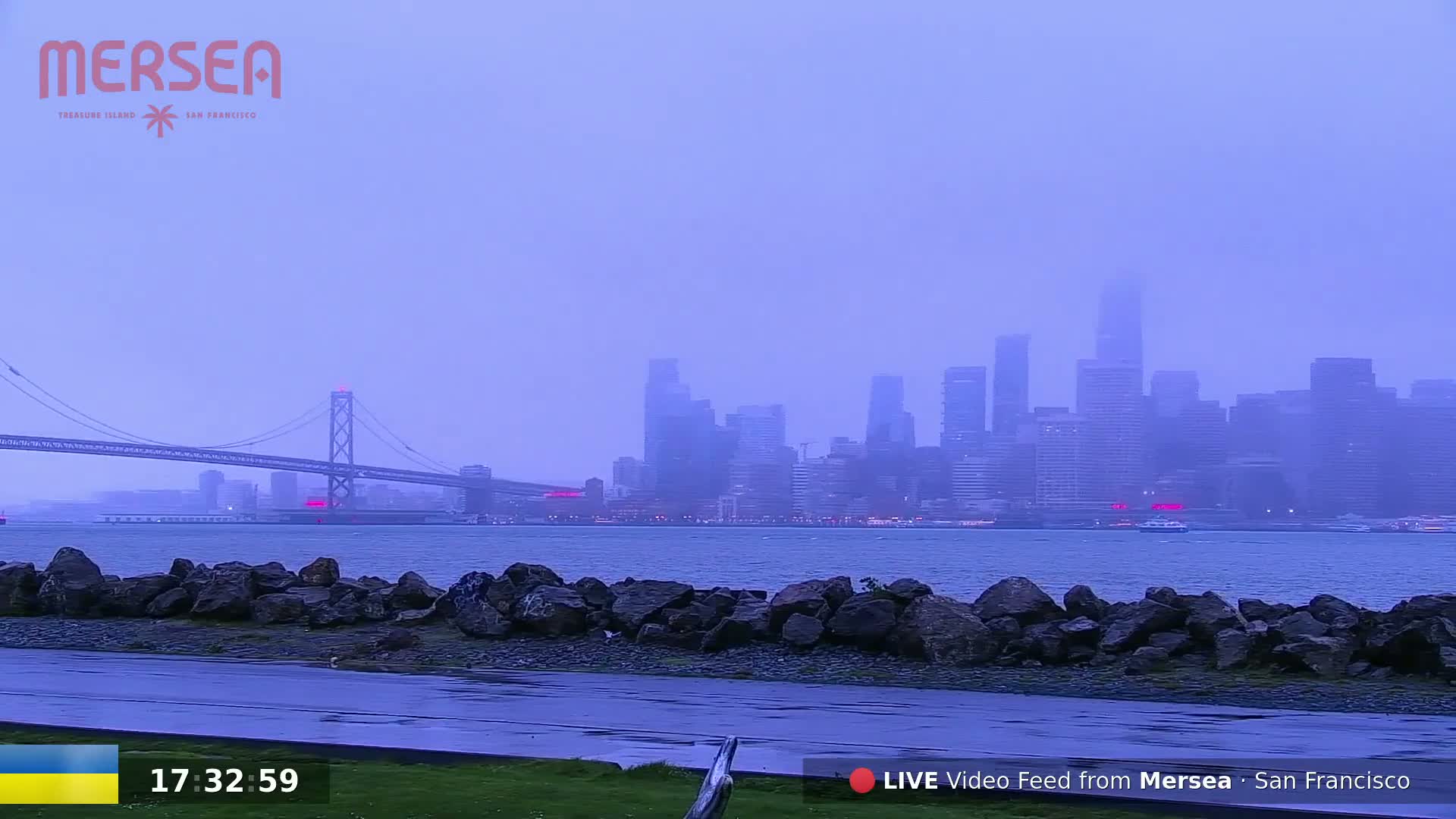 A hazy, overcast view shows a cityscape across a body of water, with a bridge in the foreground.