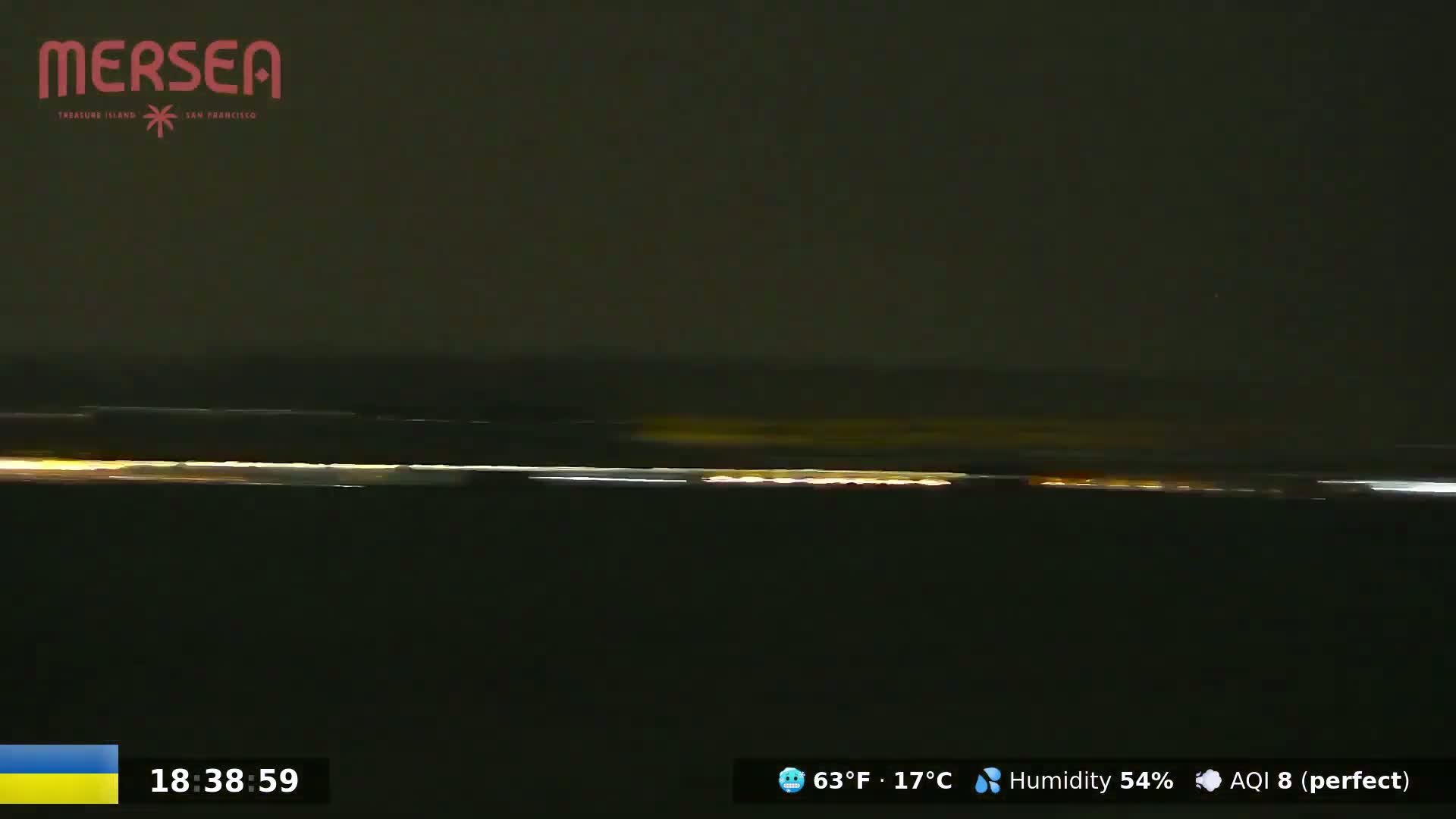 A nighttime long shot shows a dark body of water with a faint, horizontal line of lights on the horizon under a dark sky.