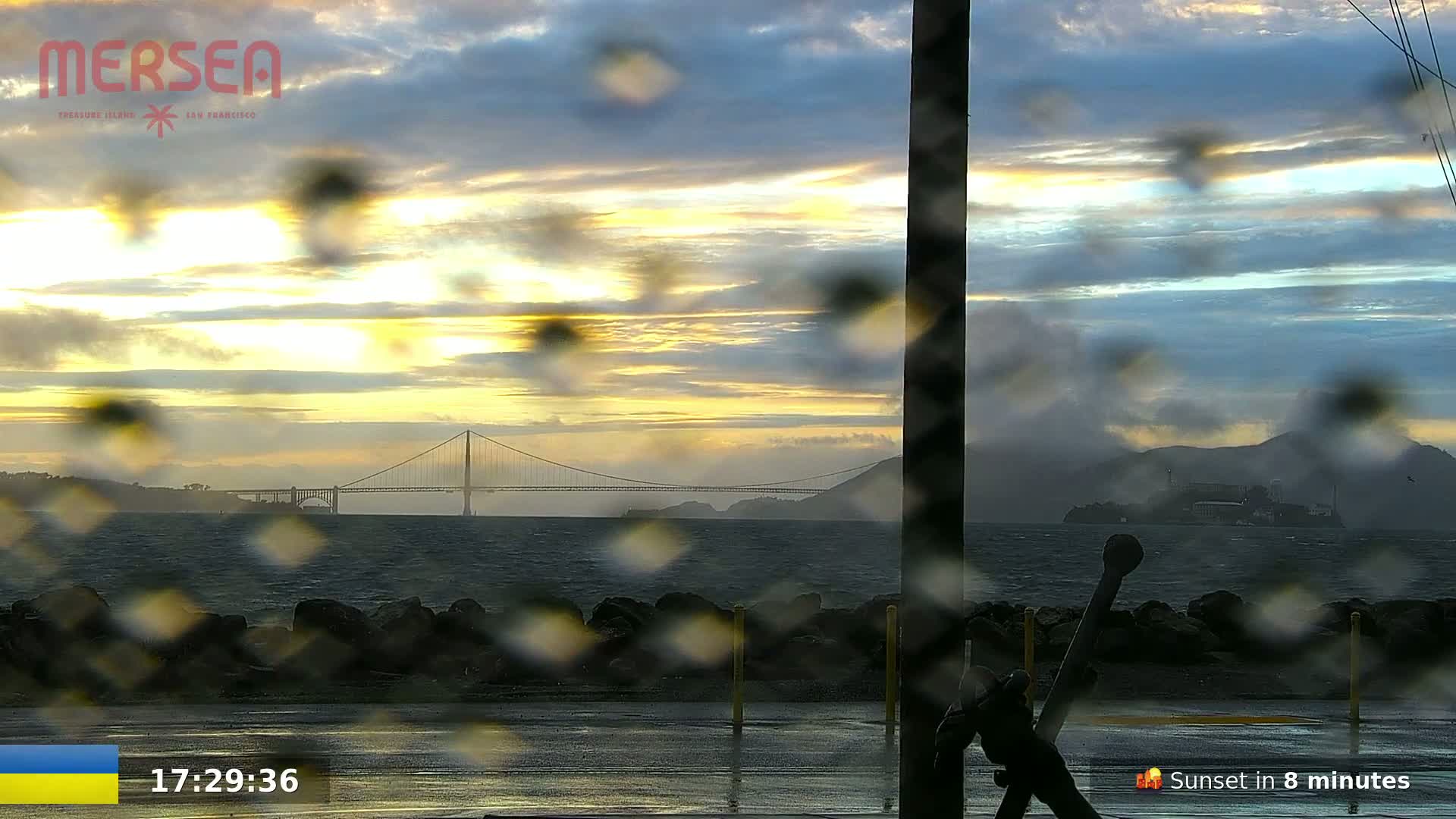 A rain-covered view of a bridge and Alcatraz Island at sunset.