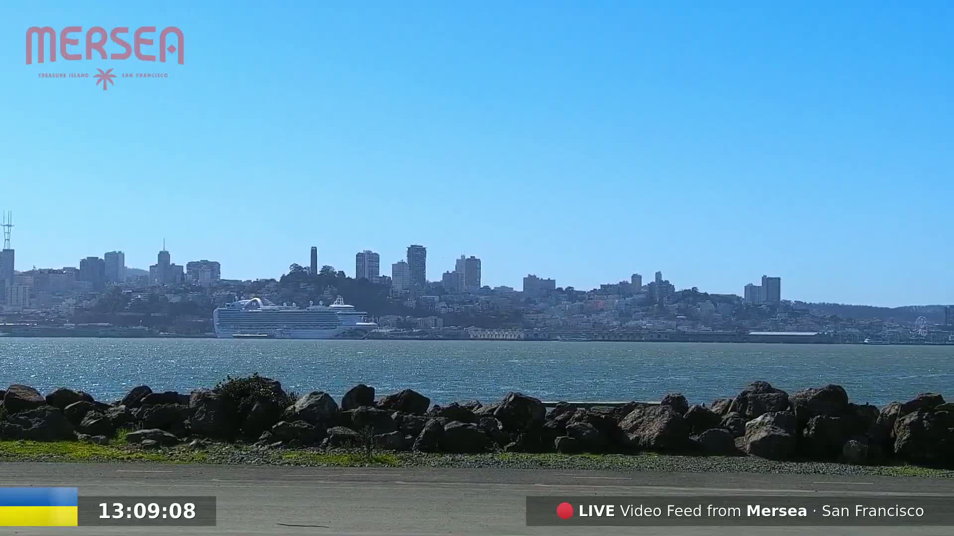 A cruise ship is in the water in front of a city skyline on a sunny day.