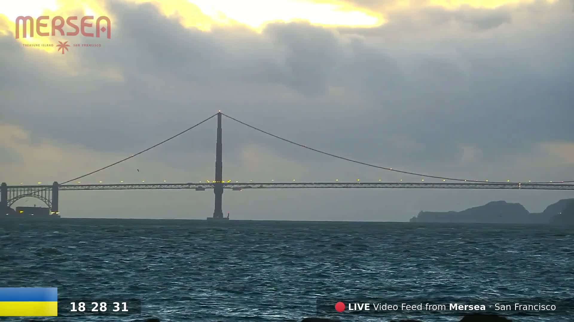 A suspension bridge spans a body of water under a cloudy, twilight sky.