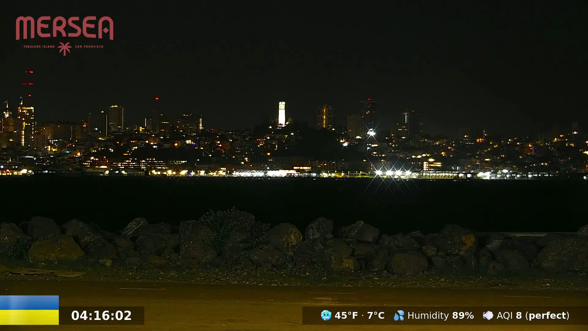 A nighttime view of a city skyline across a body of water, with a tall tower prominently featured in the center, under a clear, dark sky.