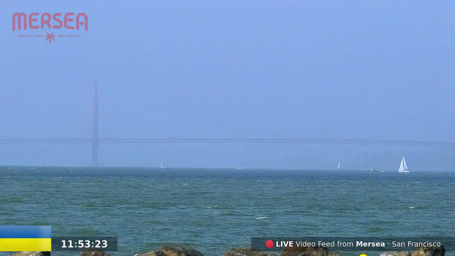 A hazy, distant view of a bridge over a body of water with several sailboats visible on the horizon.