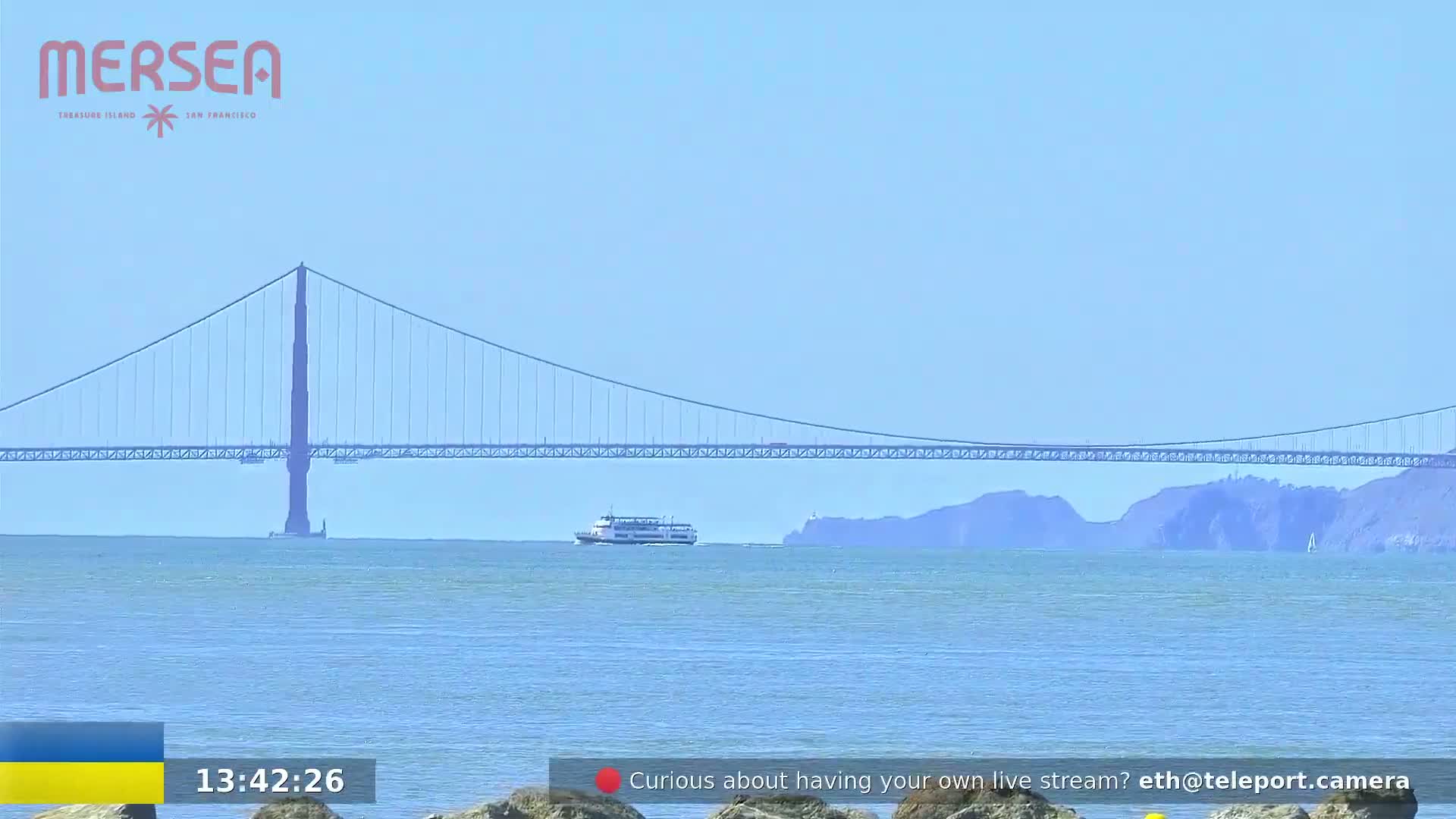 A ferry sails in front of a suspension bridge on a calm, sunny day.