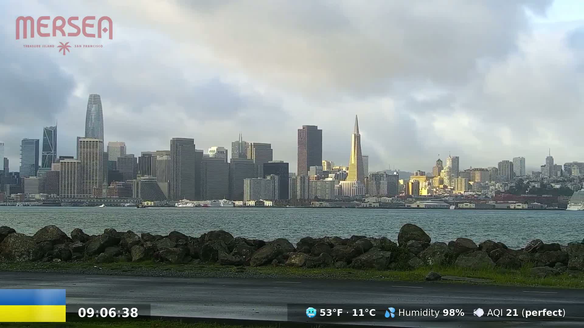 A city skyline, including several skyscrapers and the Transamerica Pyramid, is visible across a body of water under a cloudy sky.