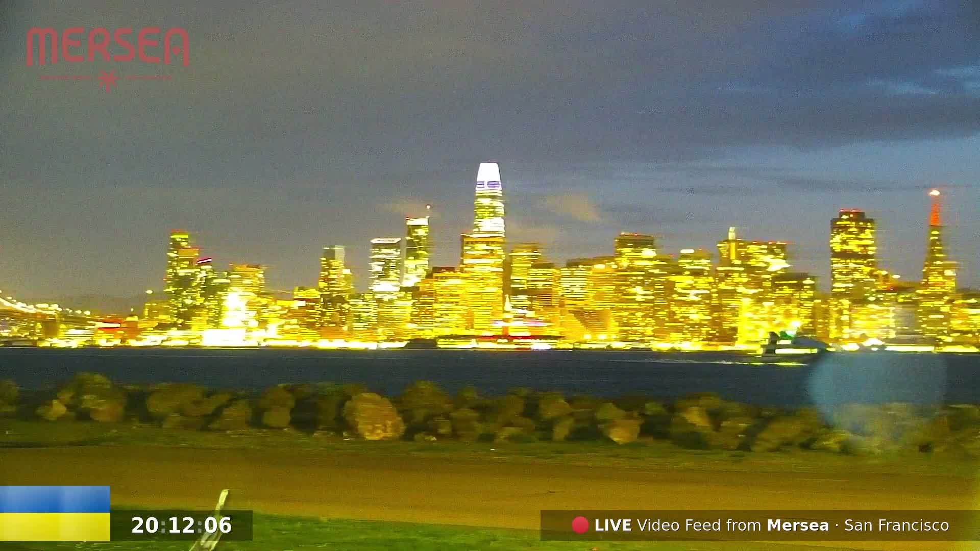 A nighttime view of the San Francisco skyline, illuminated by city lights, across a dark body of water from a low vantage point.