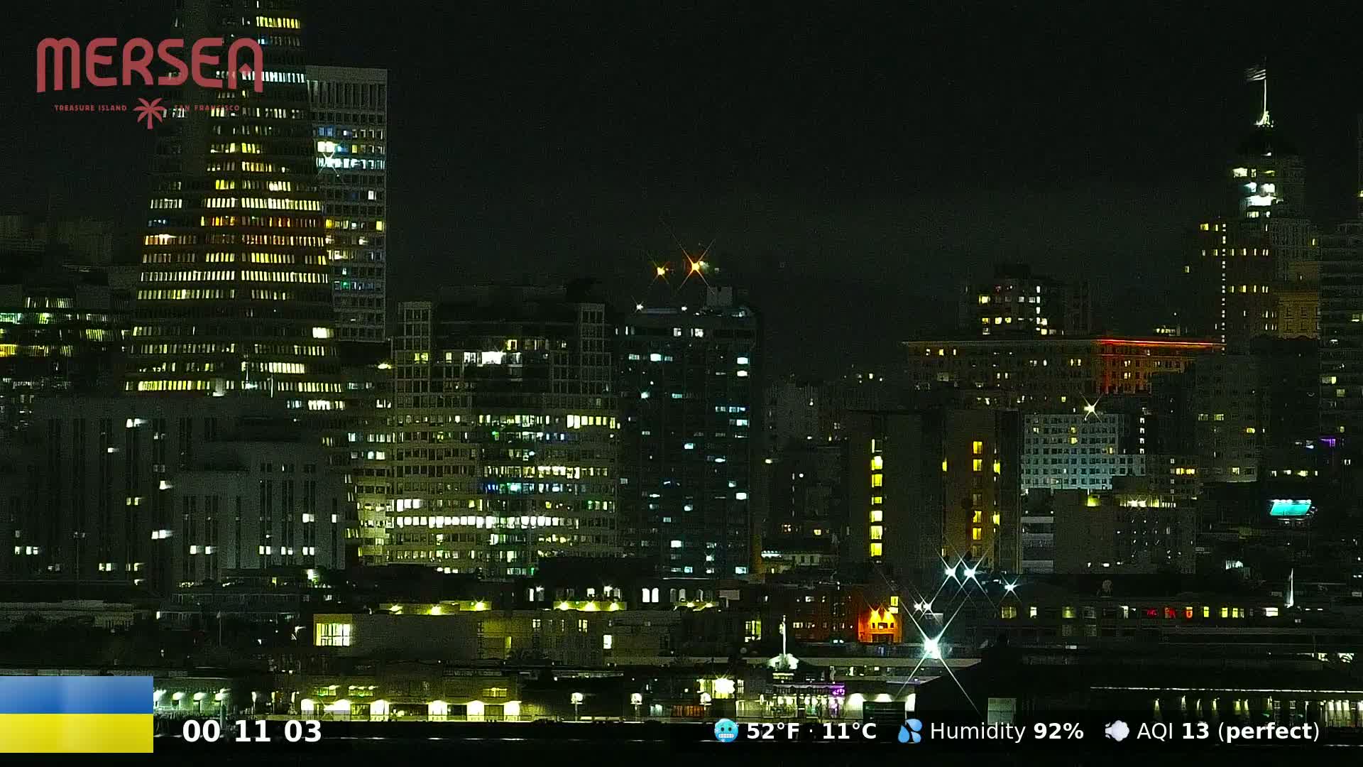 A nighttime cityscape of illuminated buildings under a dark, humid sky.