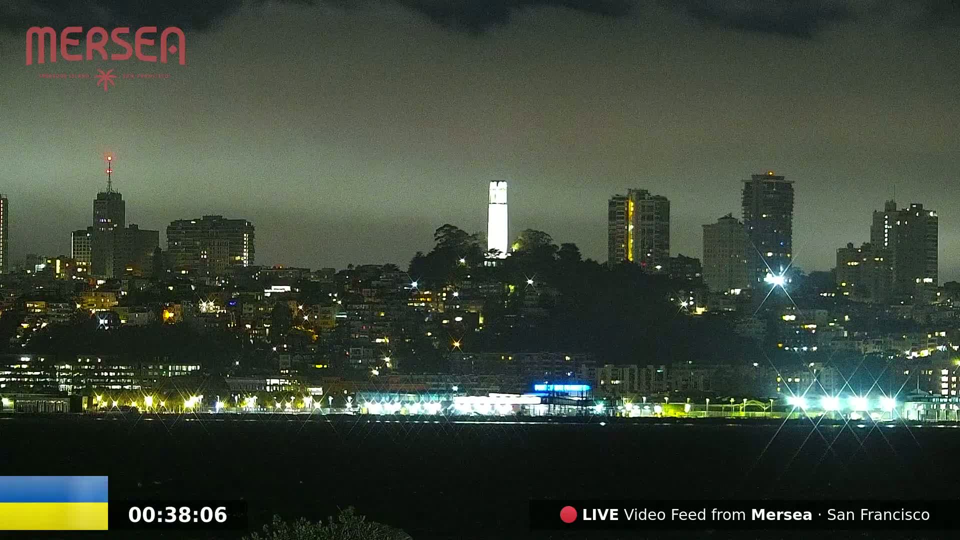 A nighttime cityscape with a prominent tower lit up, under a cloudy sky.