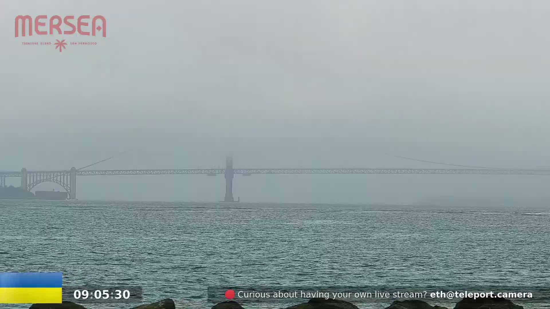A long bridge is visible across a body of water on a foggy day.