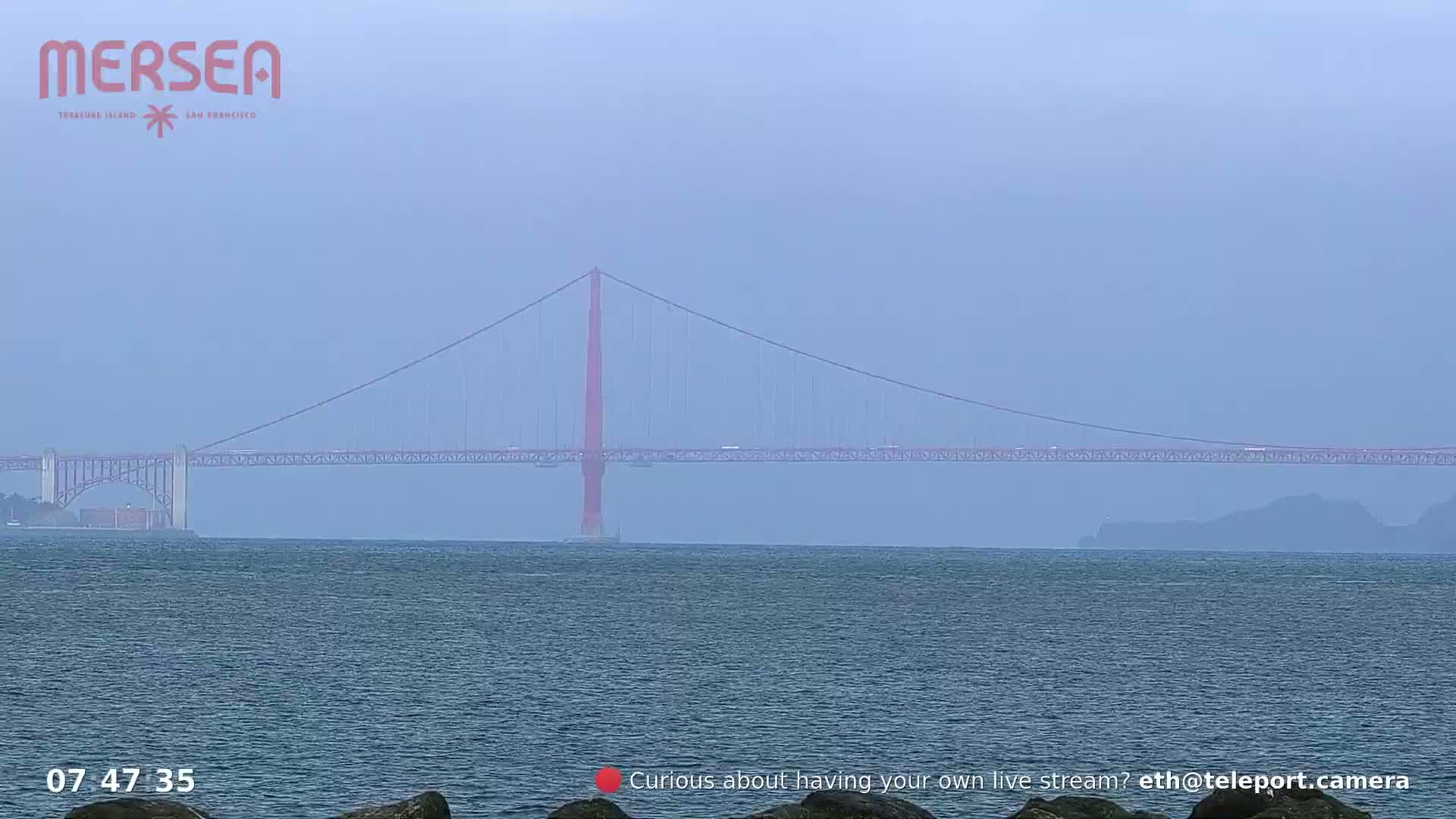 A hazy view of a suspension bridge spanning a body of water.
