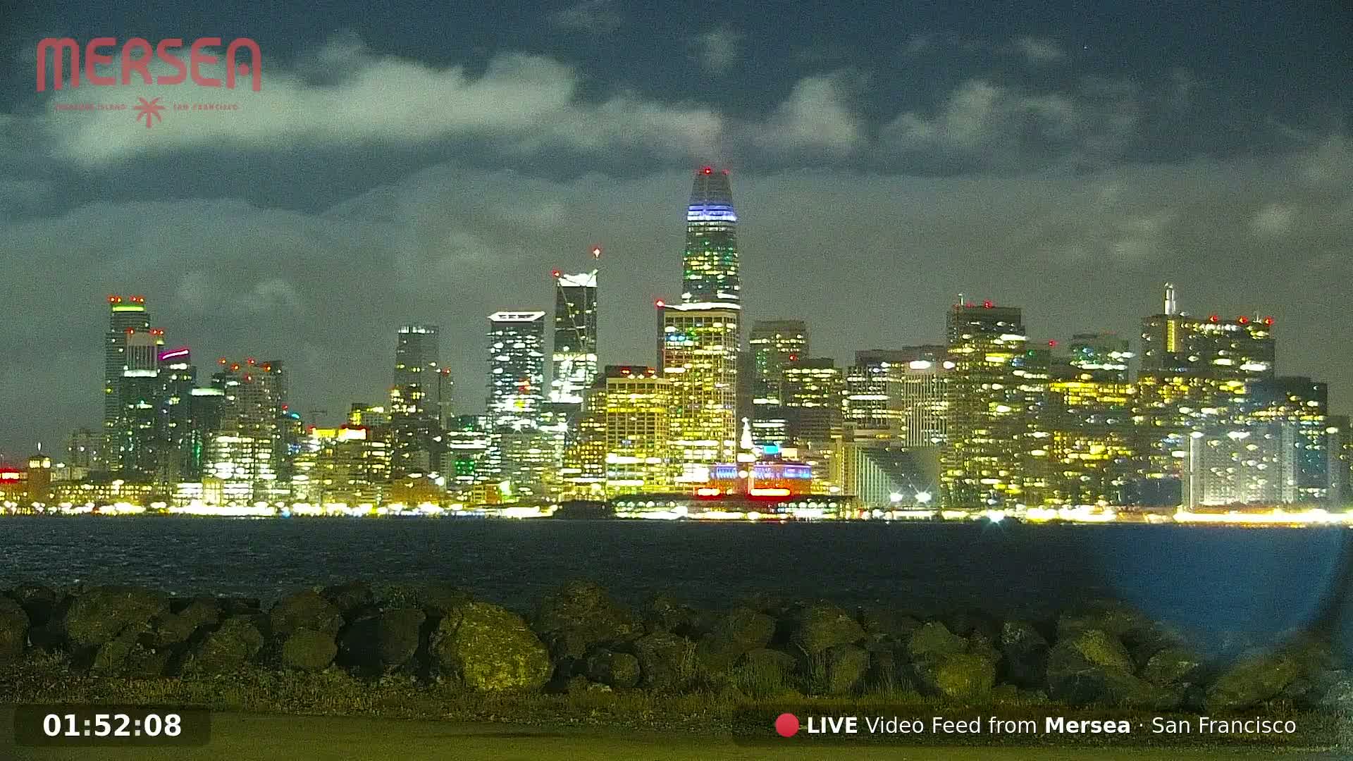 A nighttime view of a city skyline across a body of water under a cloudy sky.