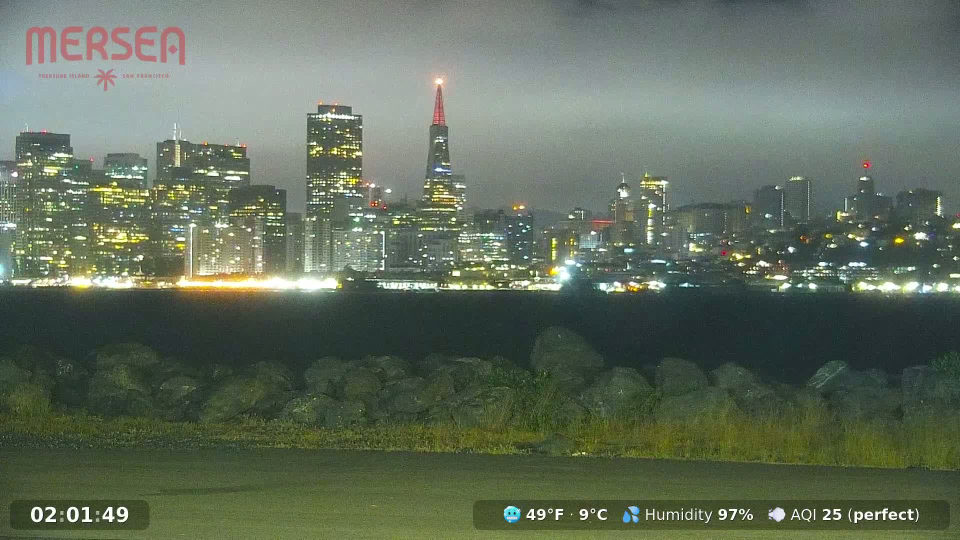 A nighttime view of a city skyline illuminated with many lights, under an overcast sky.