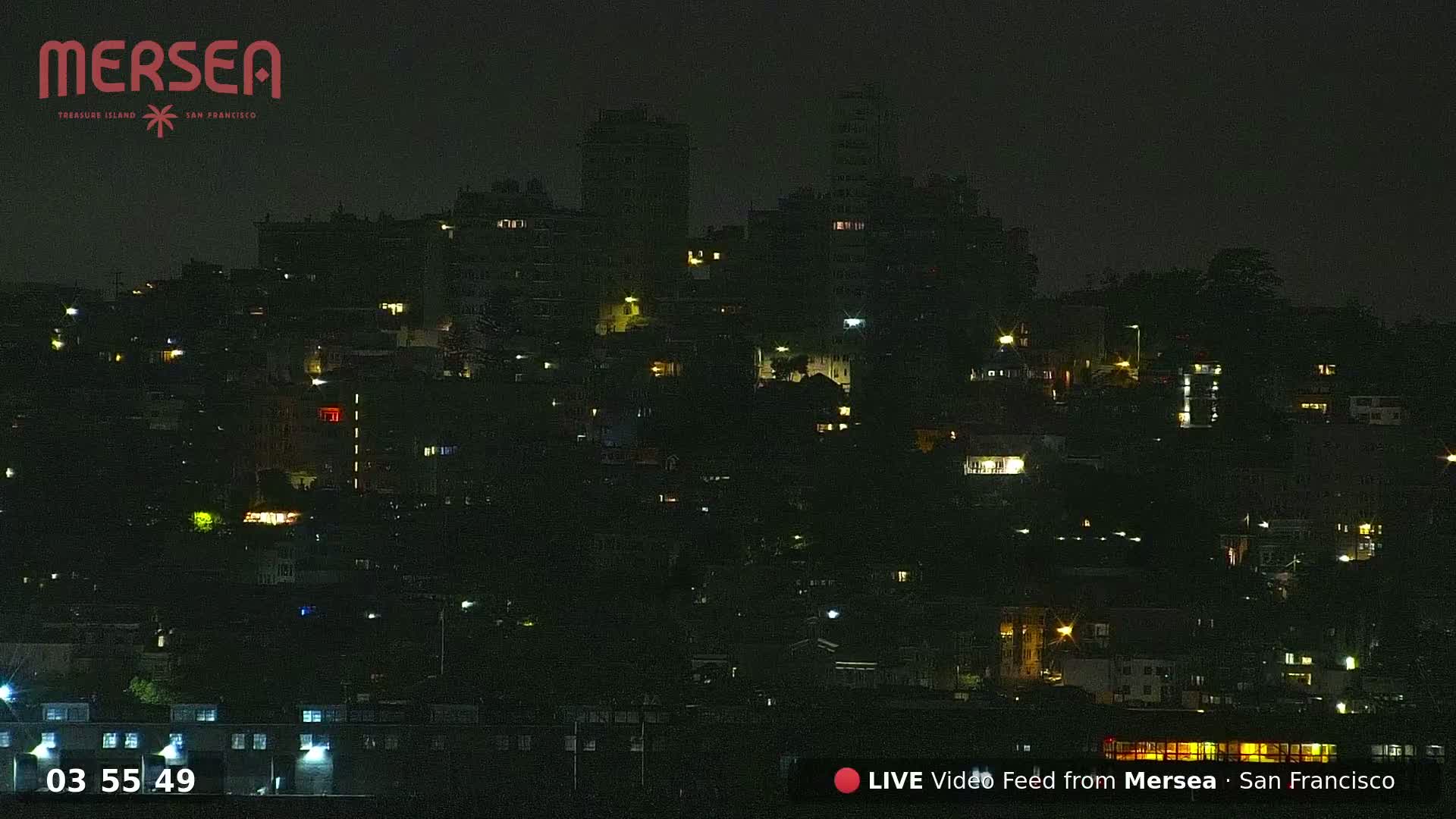 A nighttime view of a hillside city, dotted with the warm glow of lights from numerous buildings.