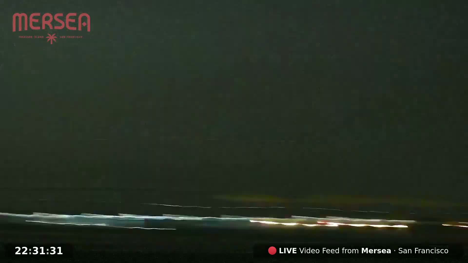 A nighttime long-exposure shot shows streaks of light from vehicles on a dark road or roadway under a dark sky.