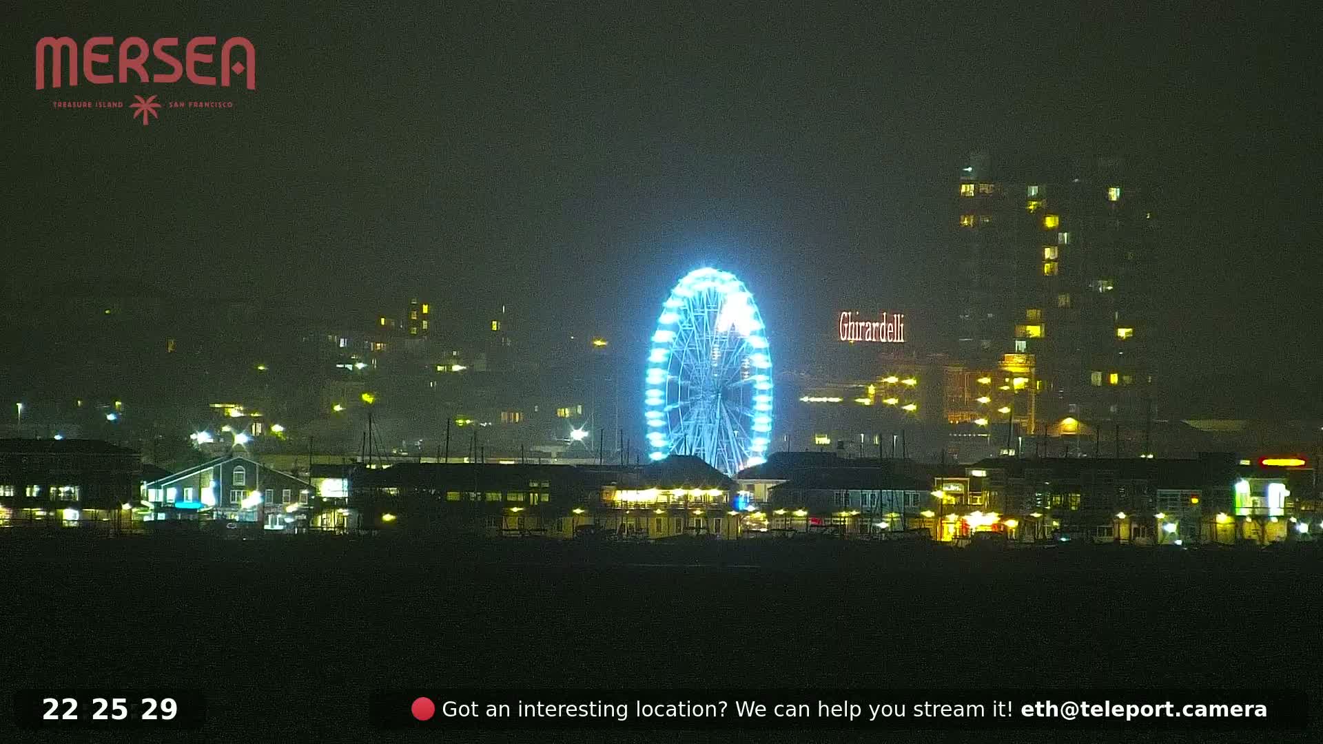 A brightly lit Ferris wheel is the focal point of a nighttime waterfront scene shrouded in fog or mist.