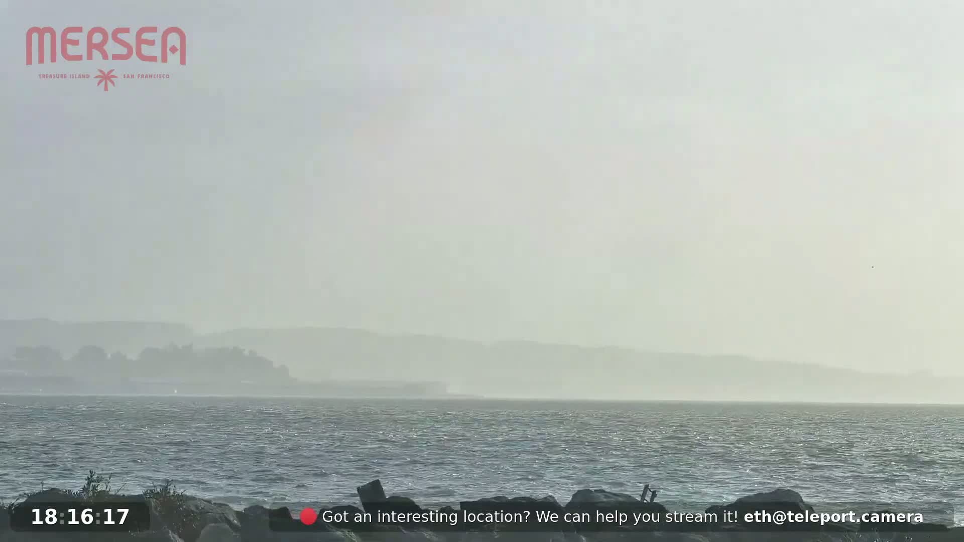 A hazy, windy day is shown over a body of water with a distant, indistinct shoreline.