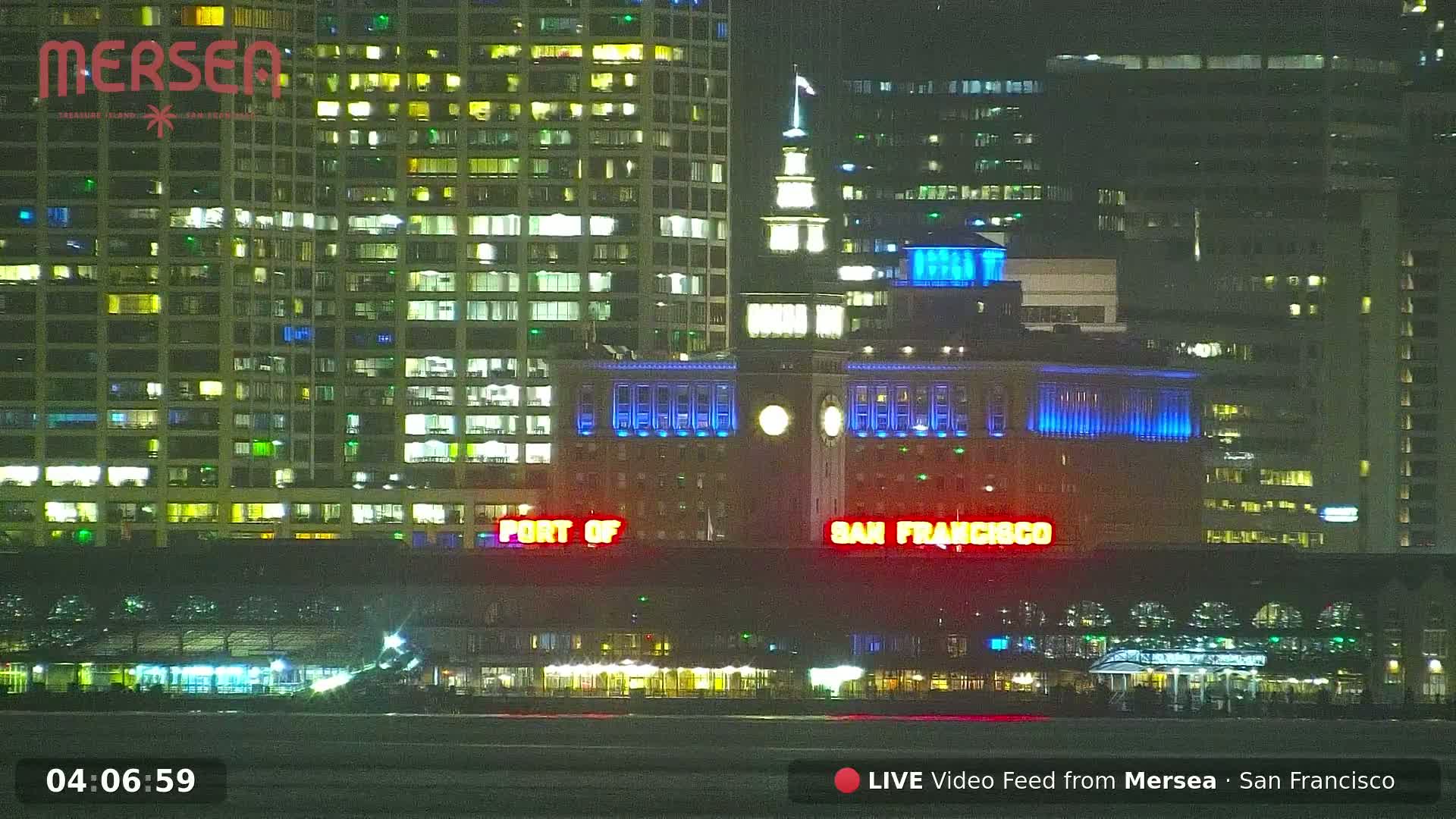 A nighttime view of illuminated buildings along a waterfront, with the "Port of San Francisco" sign visible.