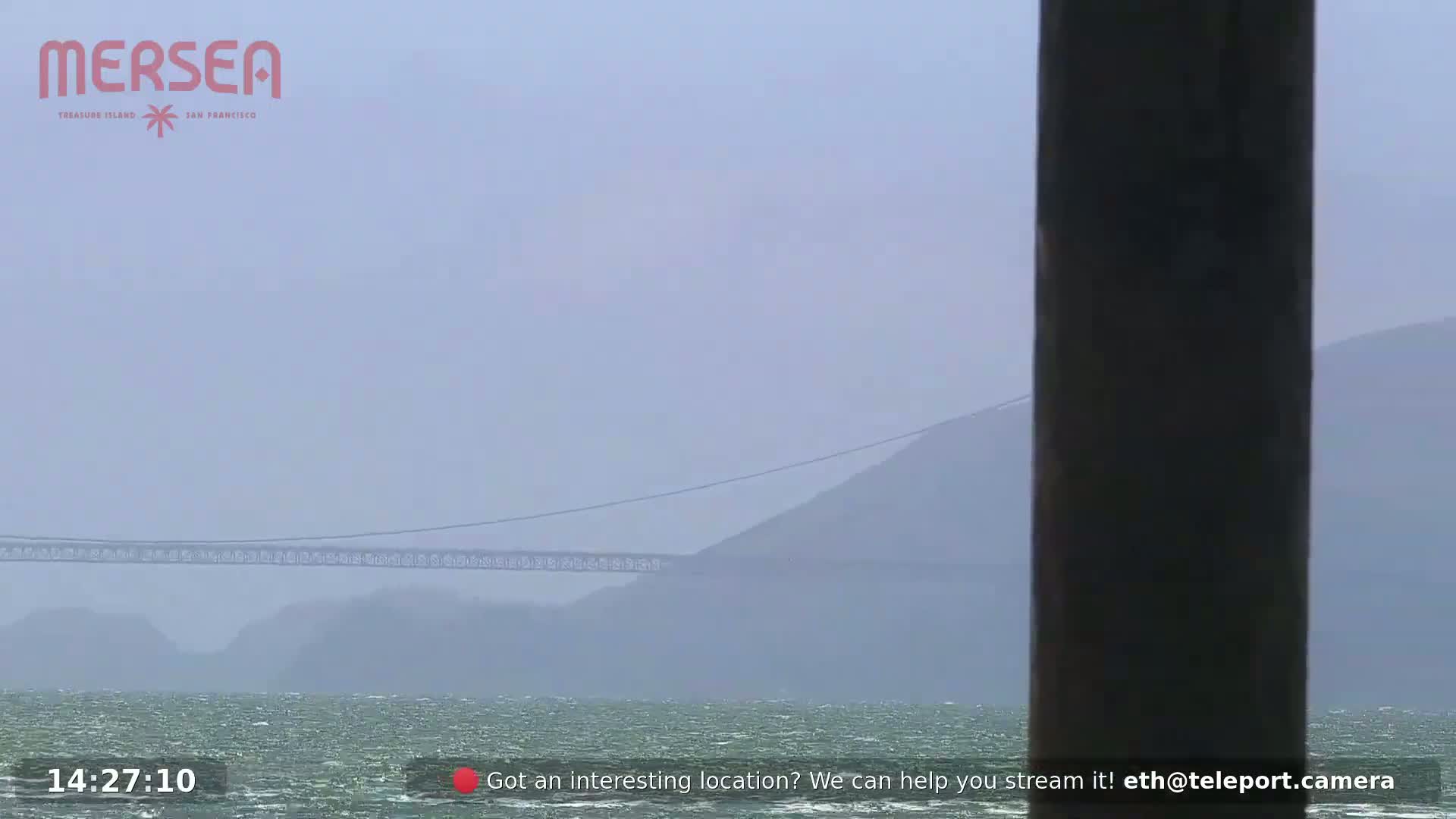 A suspension bridge is visible through hazy weather conditions over choppy water.