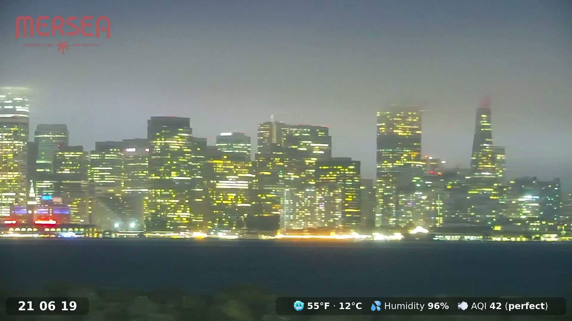 A foggy nighttime view of a city skyline with brightly lit buildings.