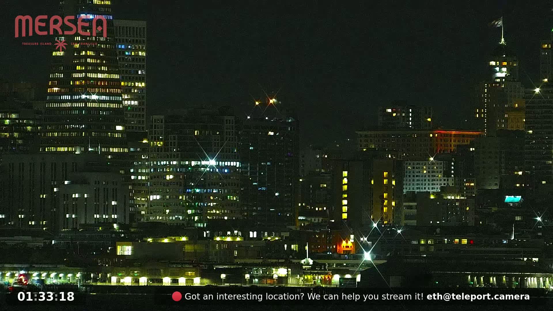 A nighttime cityscape of illuminated buildings along a waterfront.