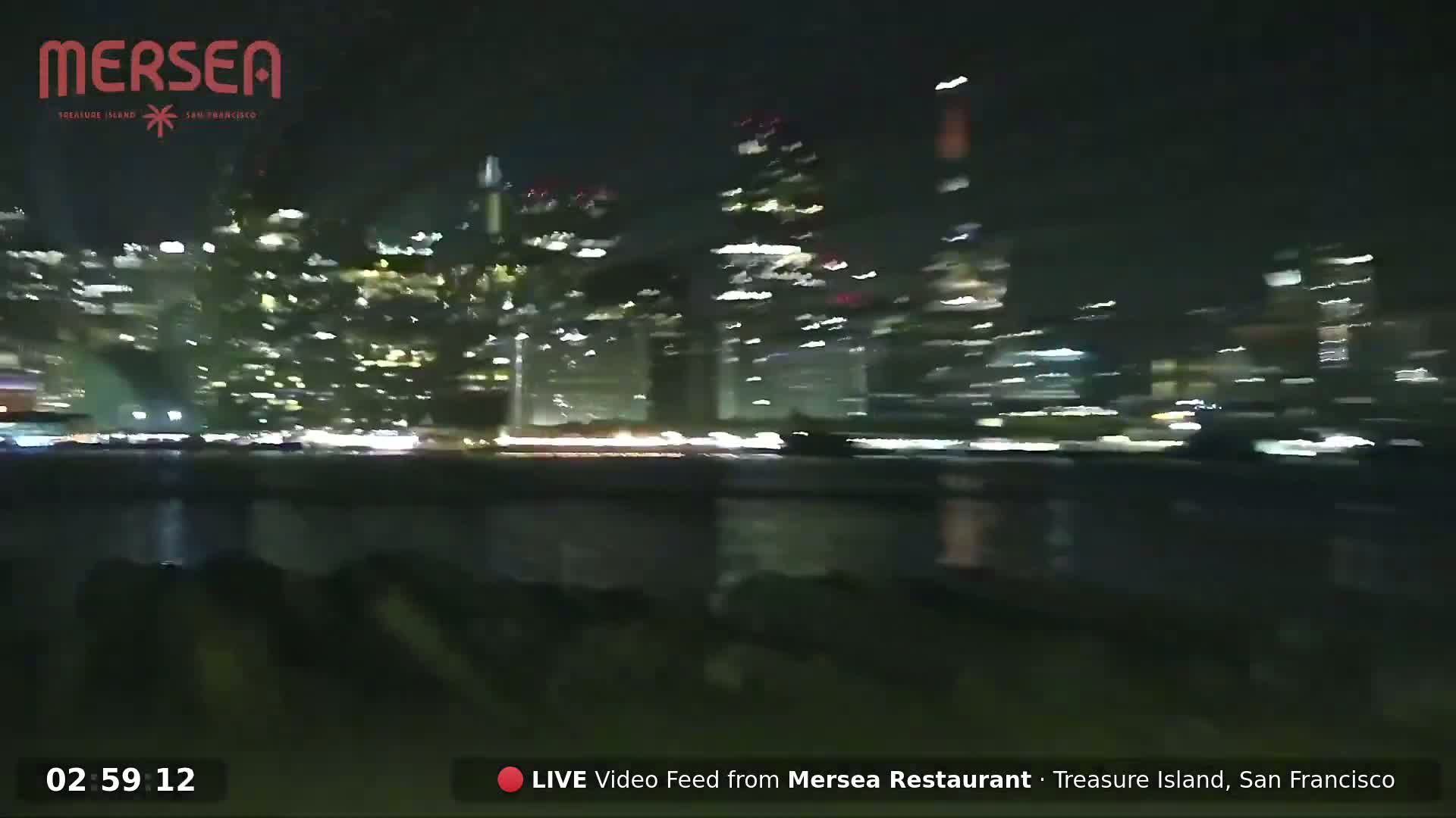 A blurry nighttime view of a city skyline across a body of water.