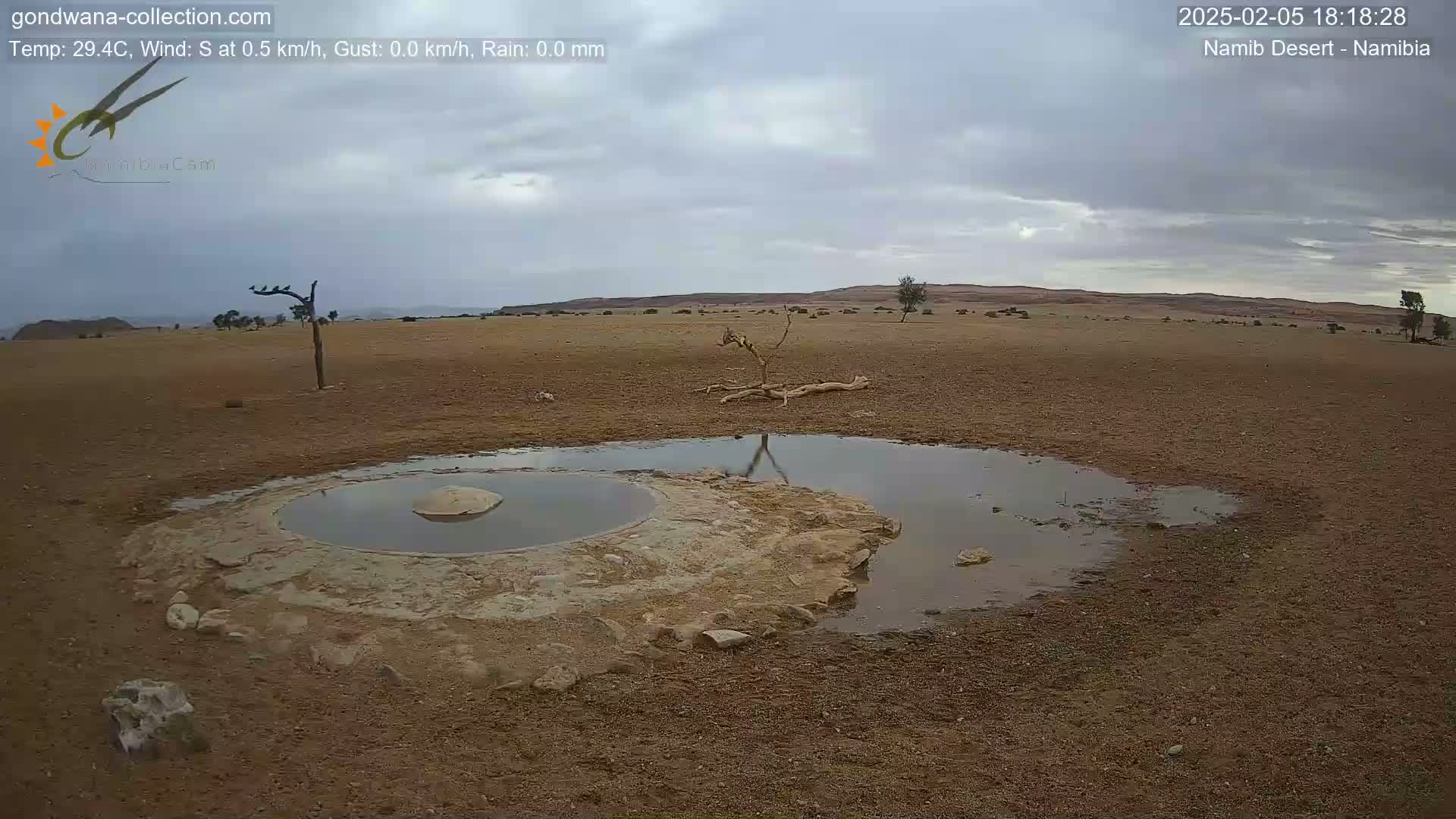 A small, shallow pool of water sits in a dry, desert landscape under a cloudy sky.