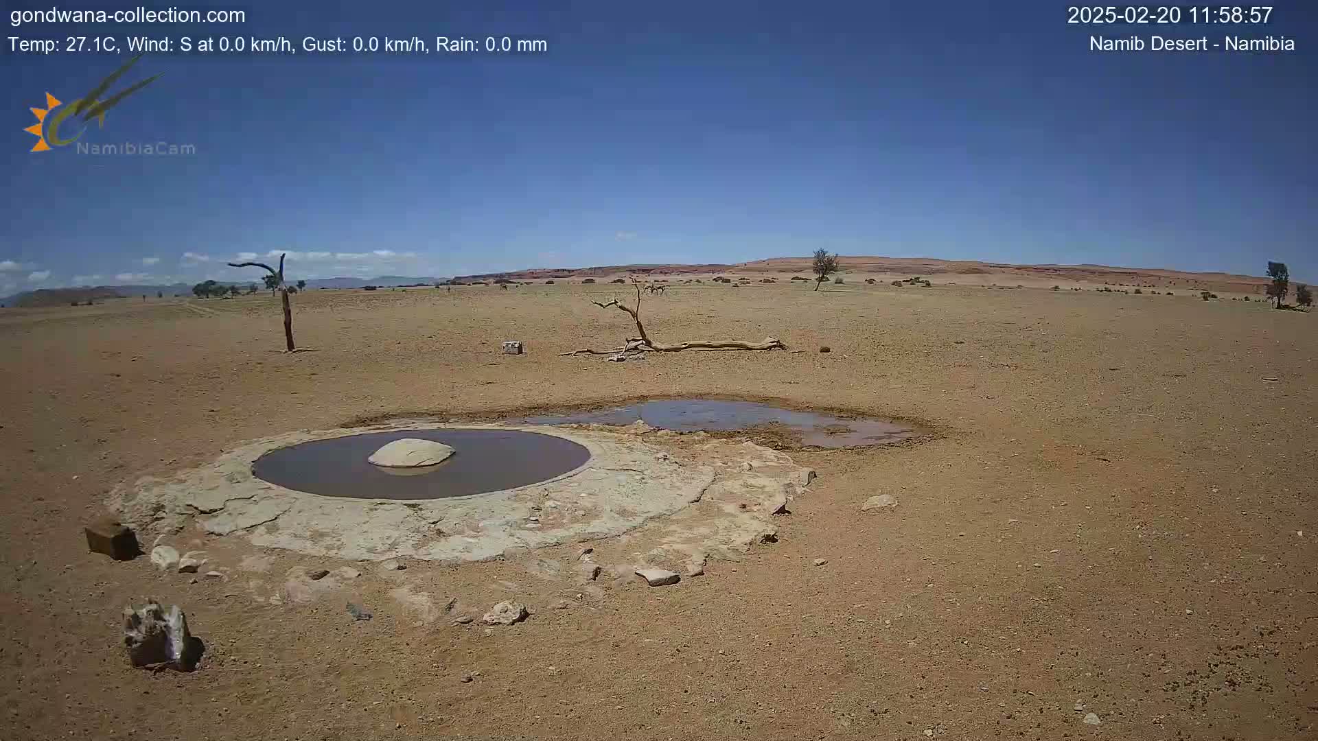 A small, shallow, circular pool of water sits in the center of a dry, arid landscape under a clear blue sky.