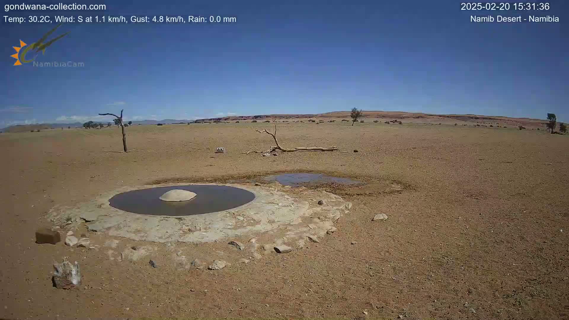 A circular, stone-lined waterhole sits in a dry, arid landscape under a clear blue sky.