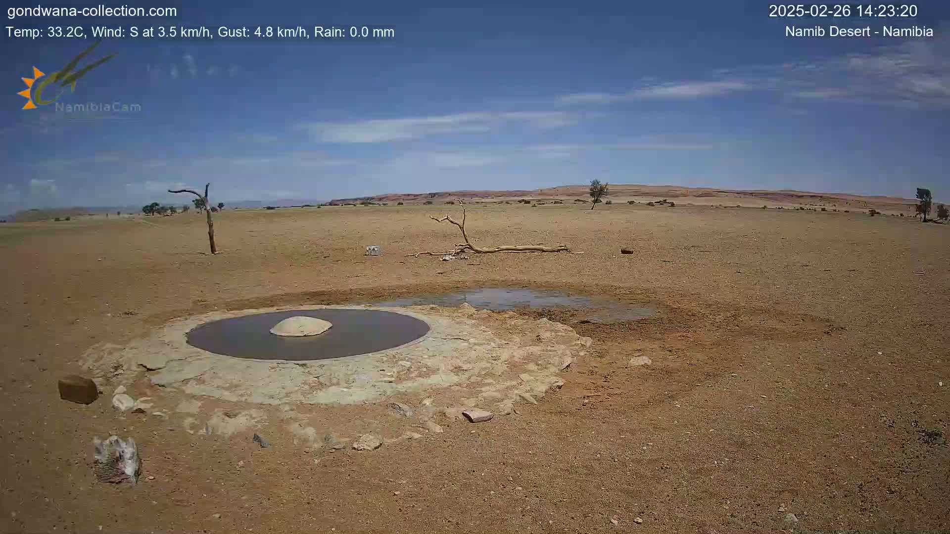A small, dark pool of water sits in a man-made basin in a dry, arid landscape under a mostly clear blue sky.