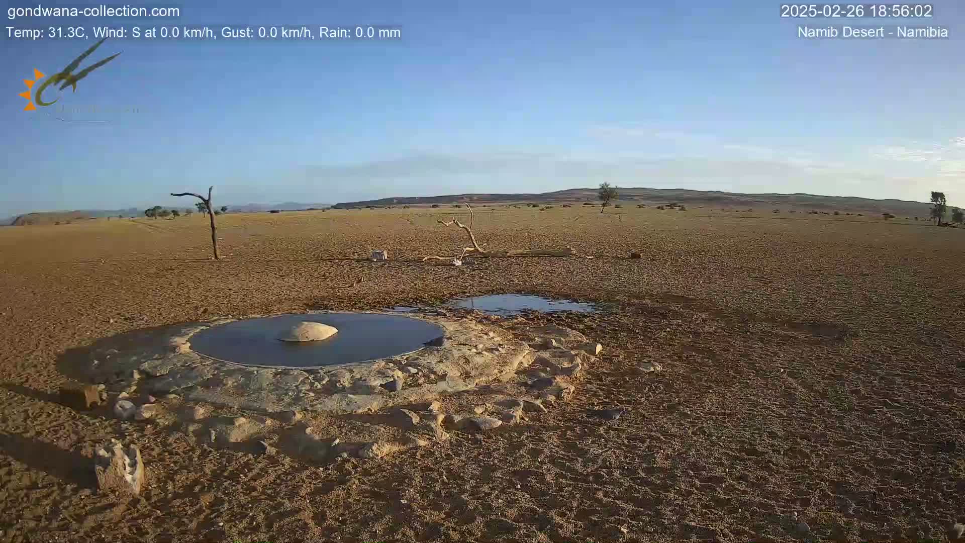 A man-made, stone-lined waterhole sits in a dry, sandy desert under a clear blue sky.