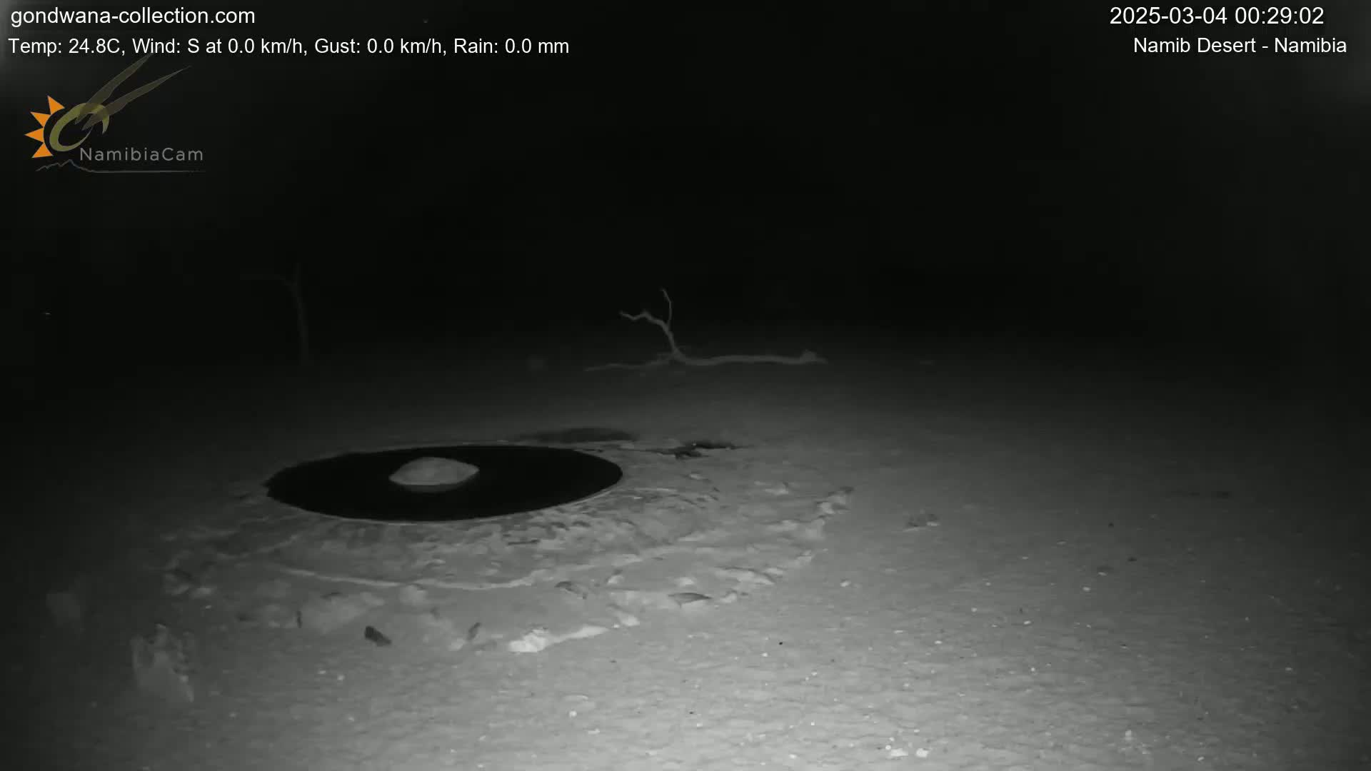 A dark, nighttime scene shows a circular, dark object on the ground surrounded by lighter-colored sand or snow under a clear sky.